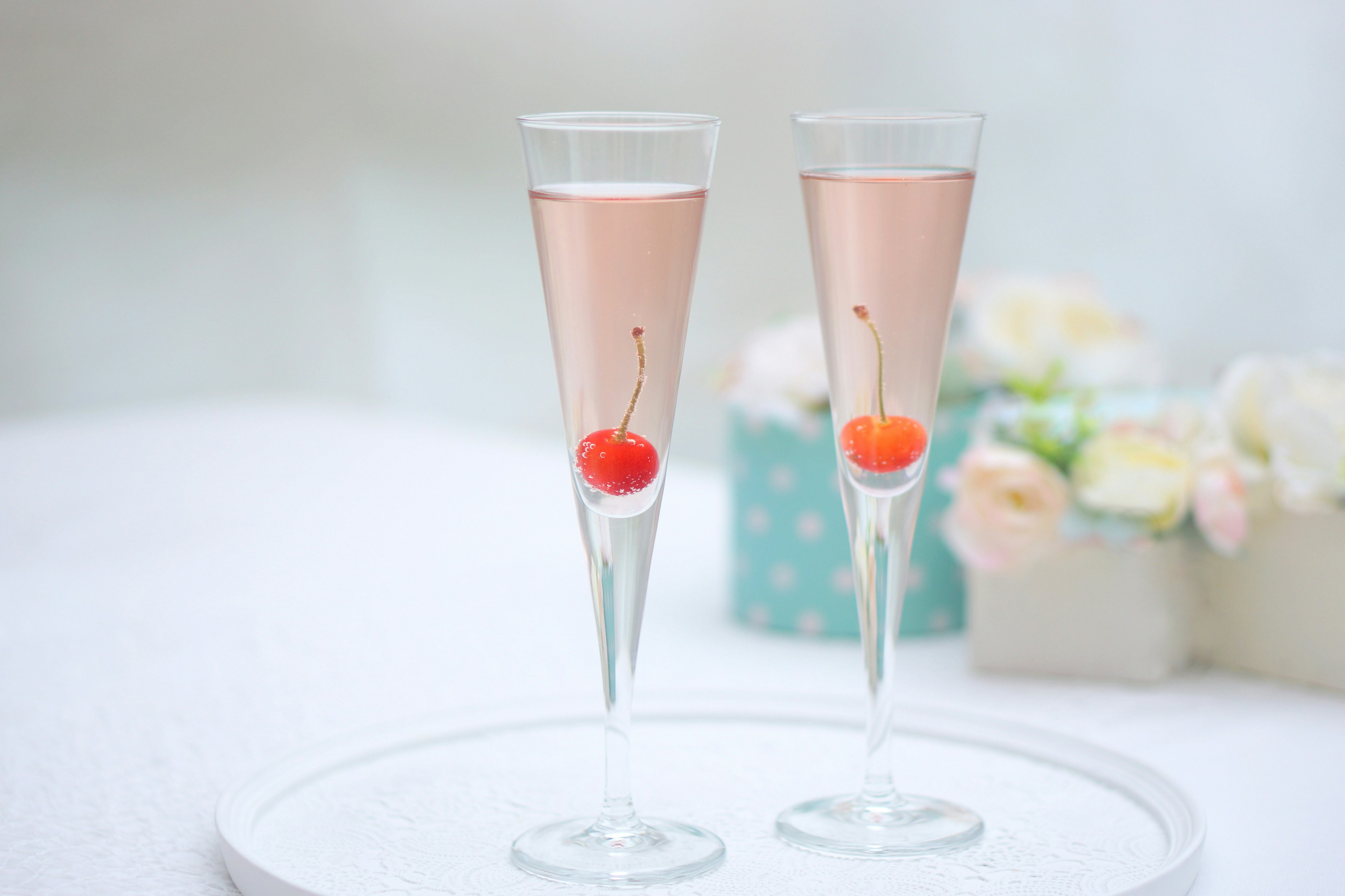 Two champagne glasses with pink beverage and red cherries