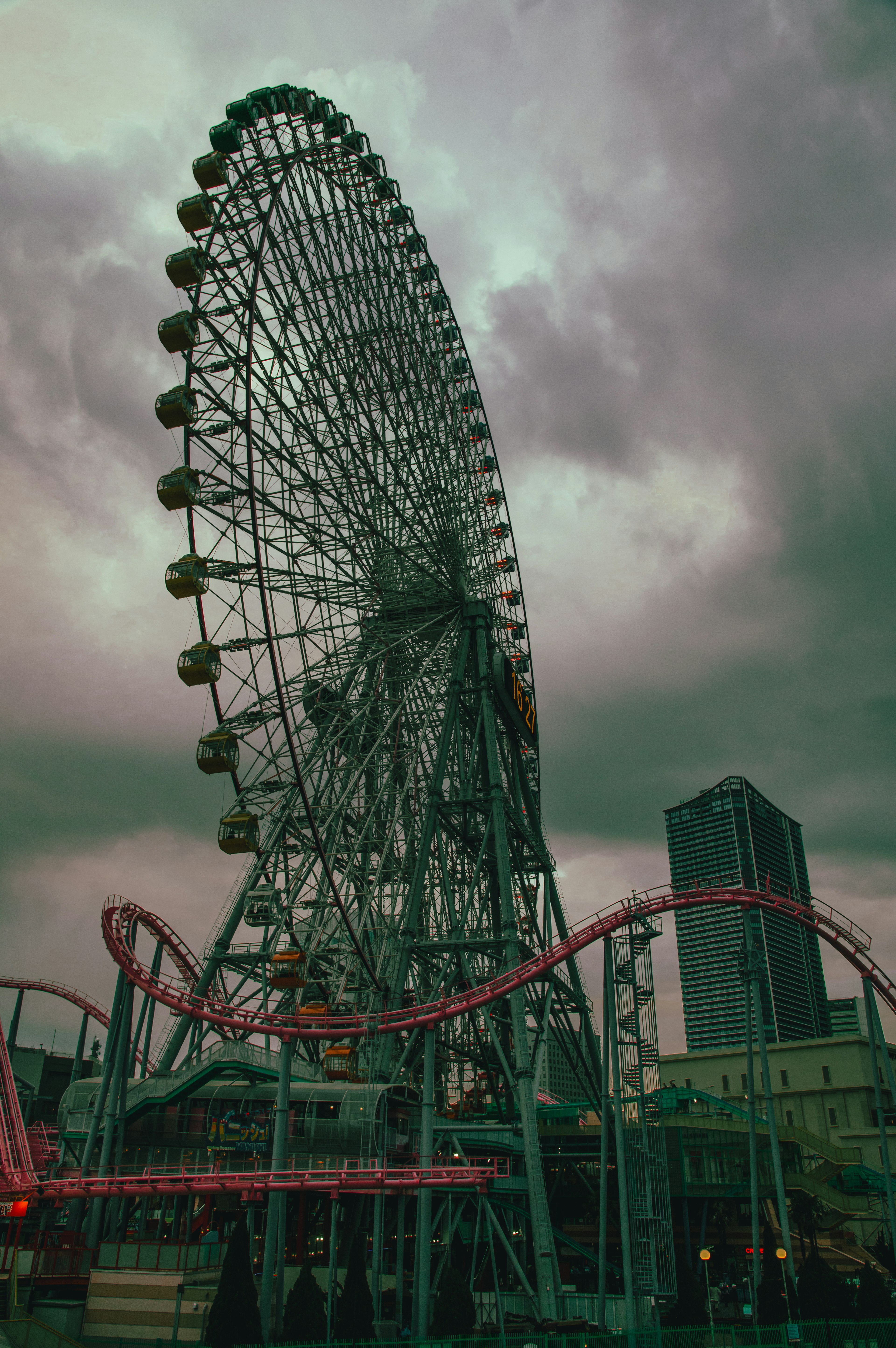 Kincir raksasa dan roller coaster di taman hiburan di bawah langit mendung