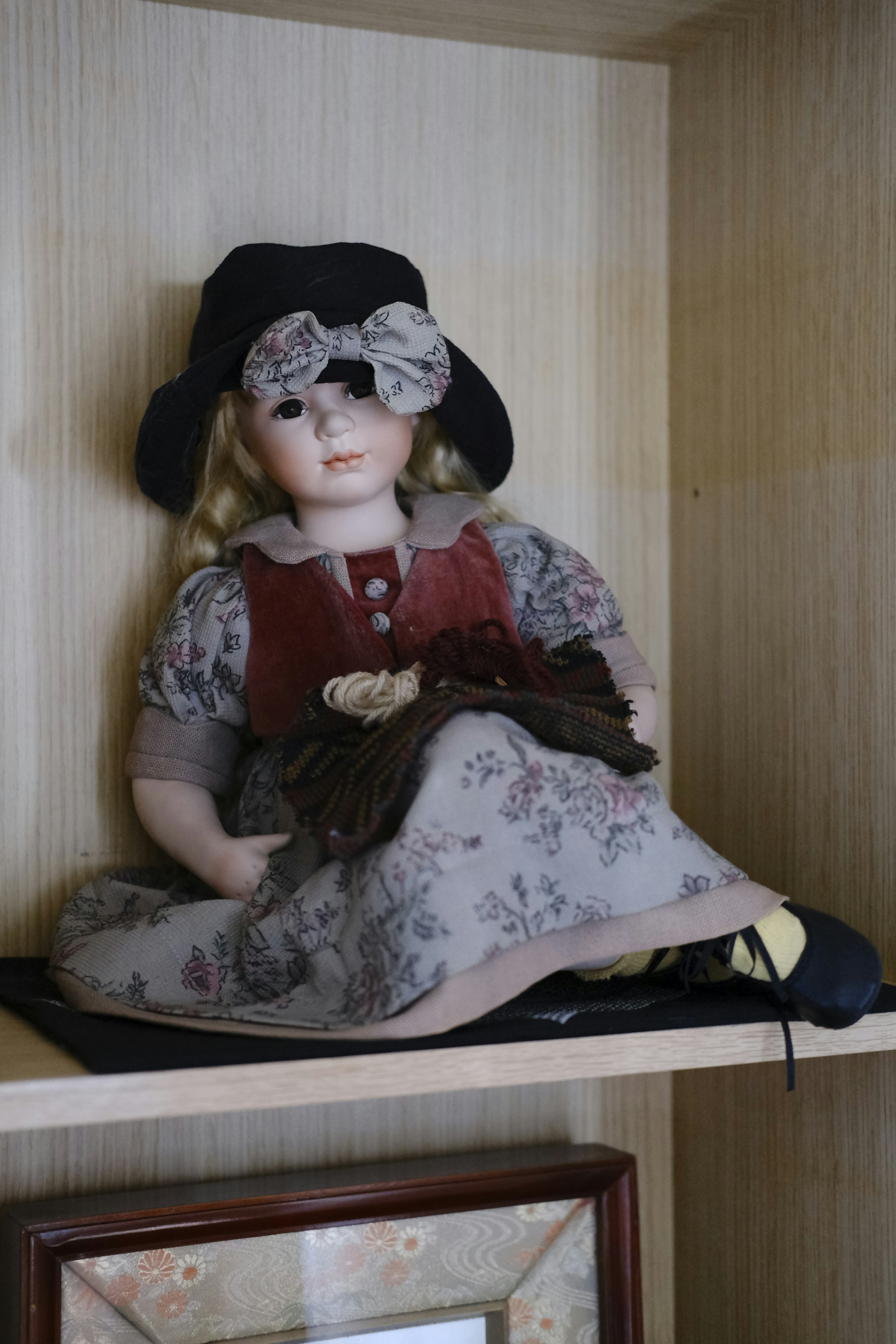 Antique doll sitting on a shelf wearing a black hat and floral dress