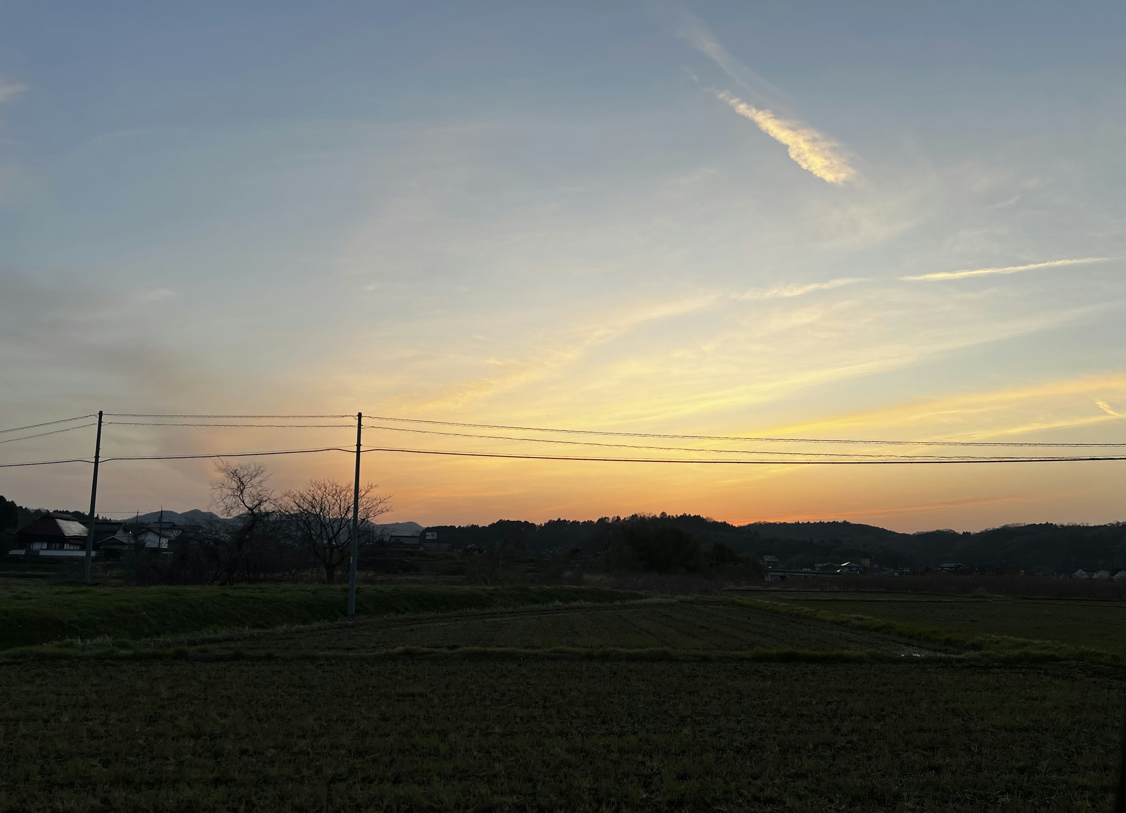 Ciel au coucher du soleil sur un paysage rural avec des lignes électriques et des collines lointaines