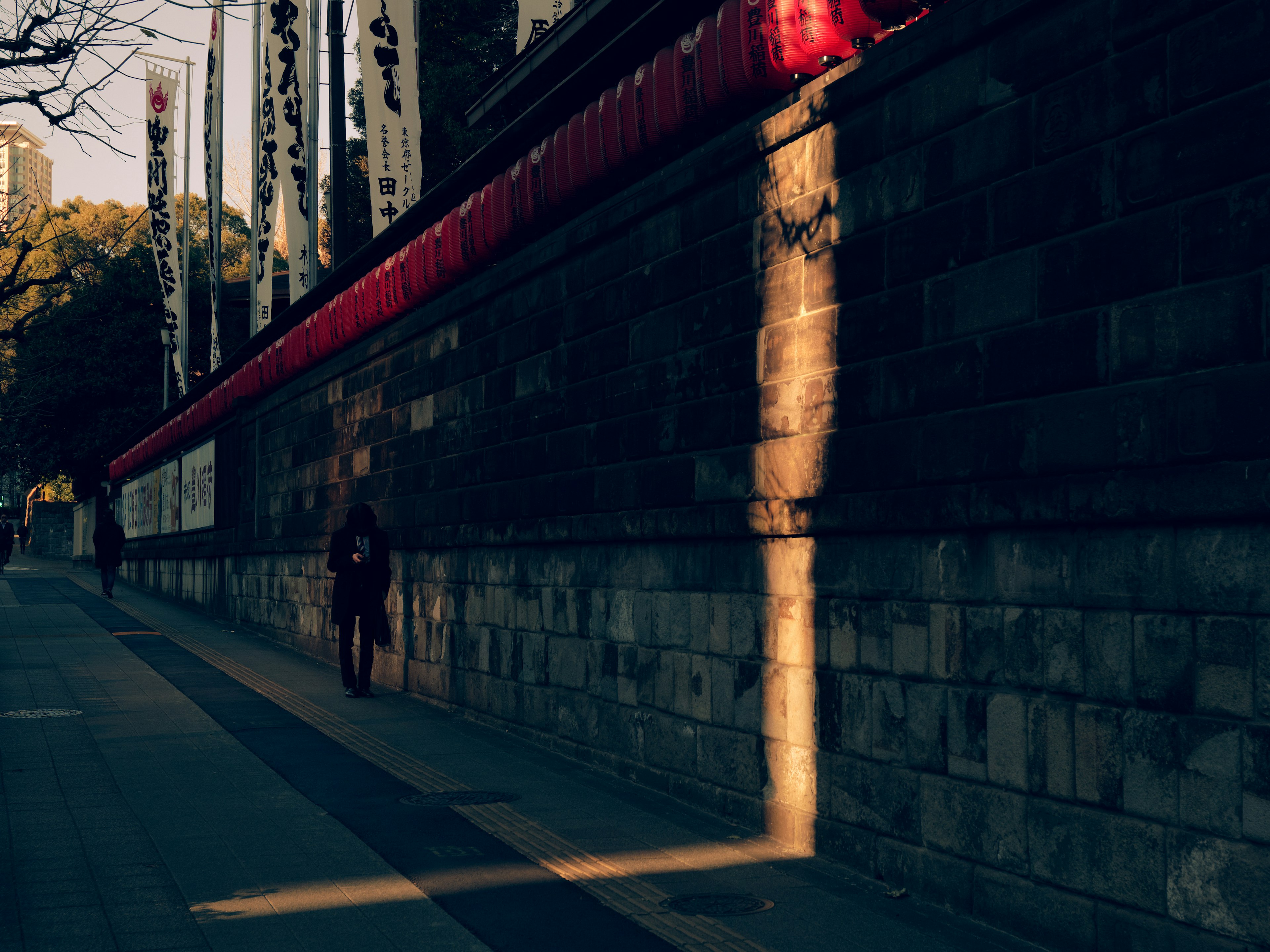 Une ombre d'une personne marchant le long d'un mur en pierre avec des lanternes rouges