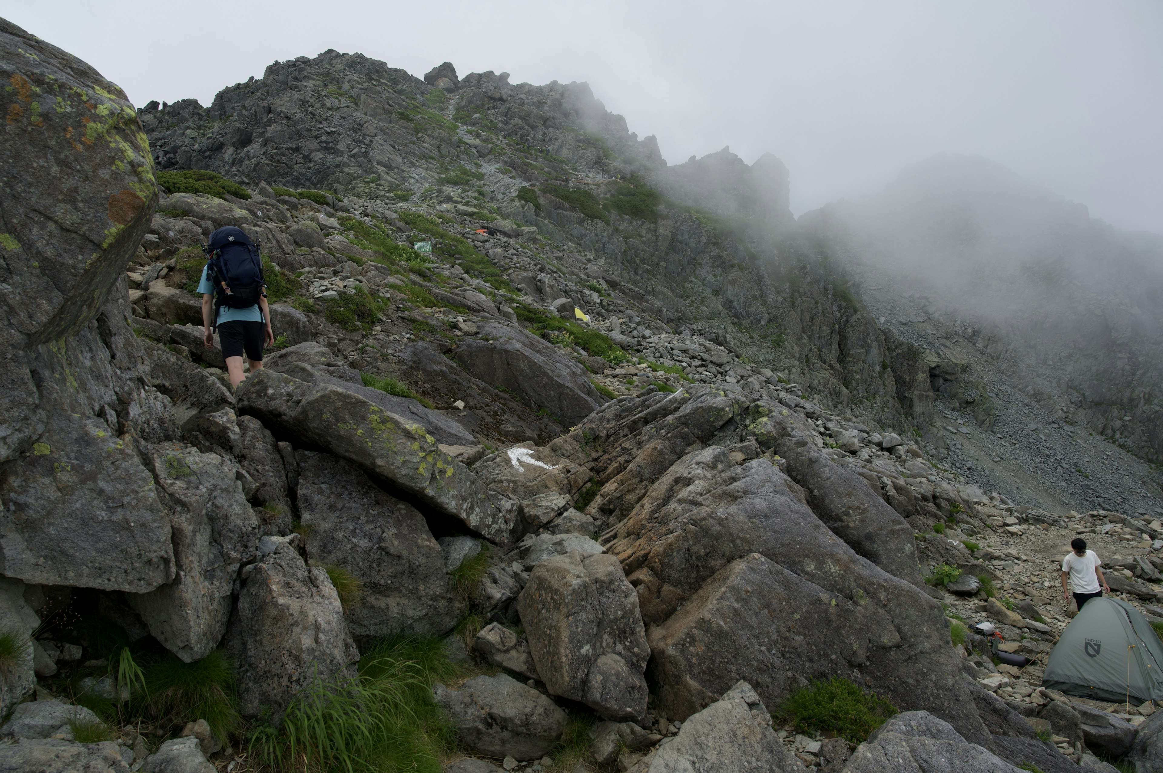 Senderista subiendo un sendero montañoso rocoso envuelto en niebla