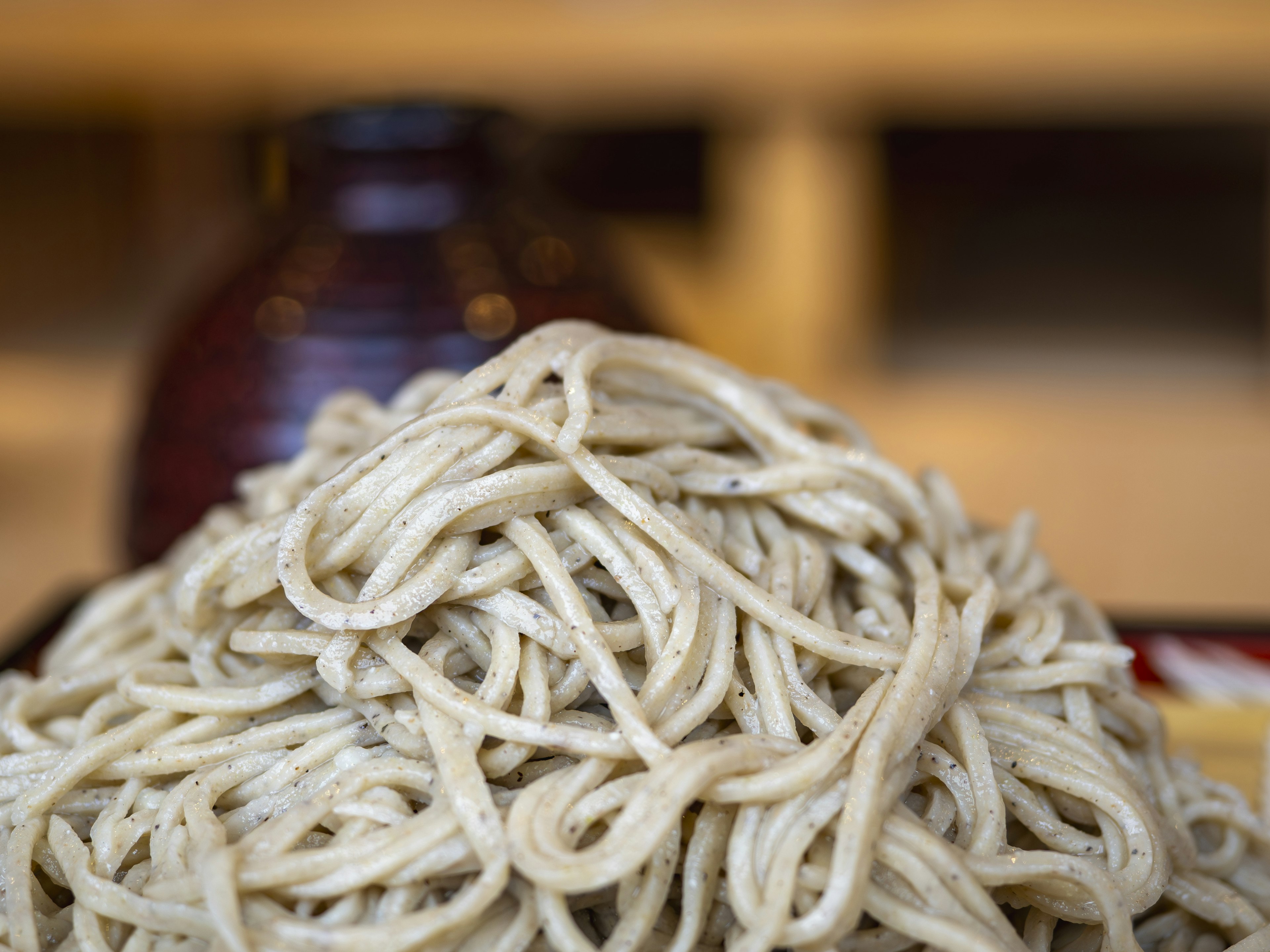 Una pila de fideos soba con una olla de salsa marrón de cerámica