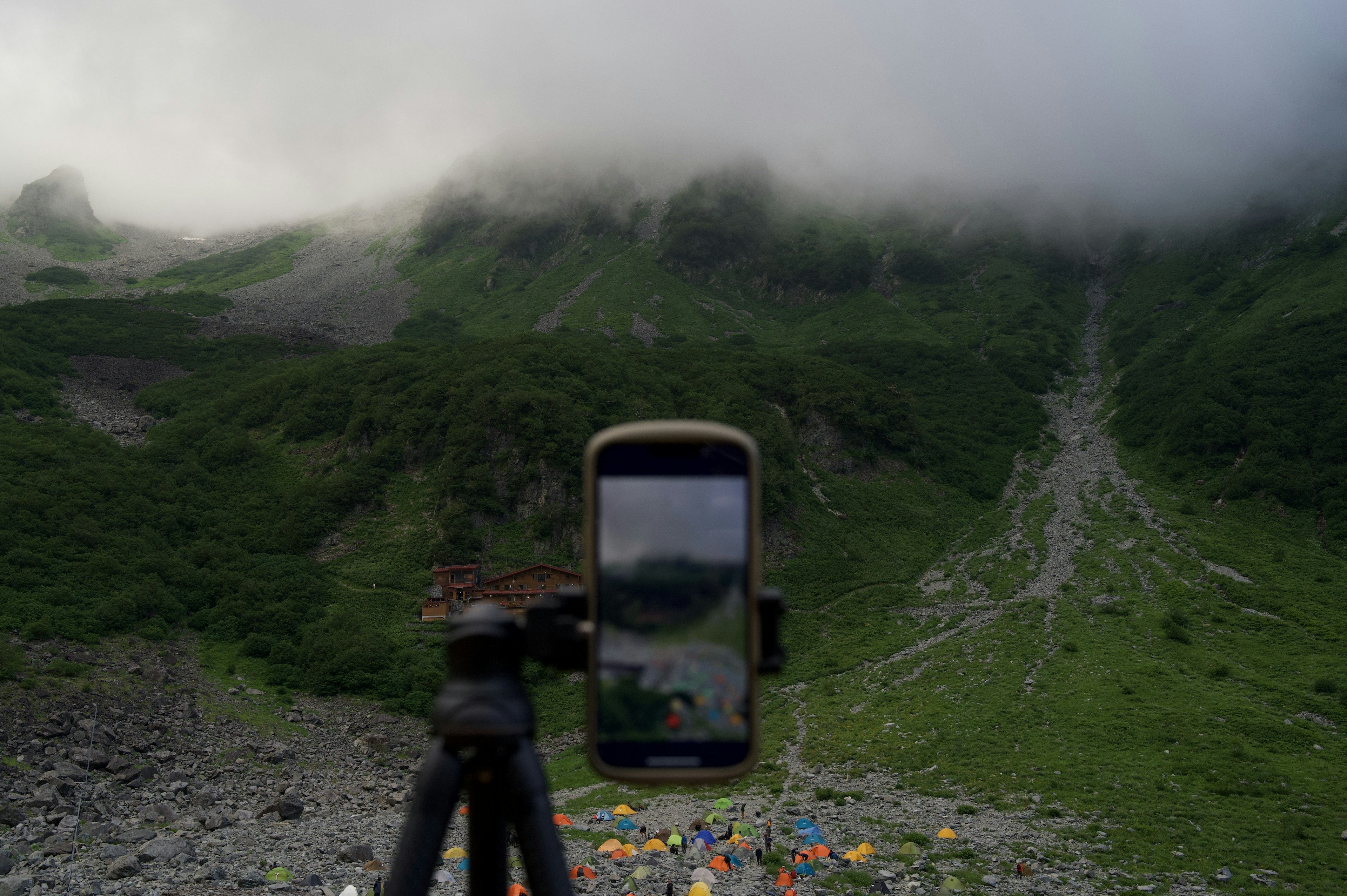 Un teléfono inteligente en un trípode capturando un paisaje montañoso cubierto de nubes