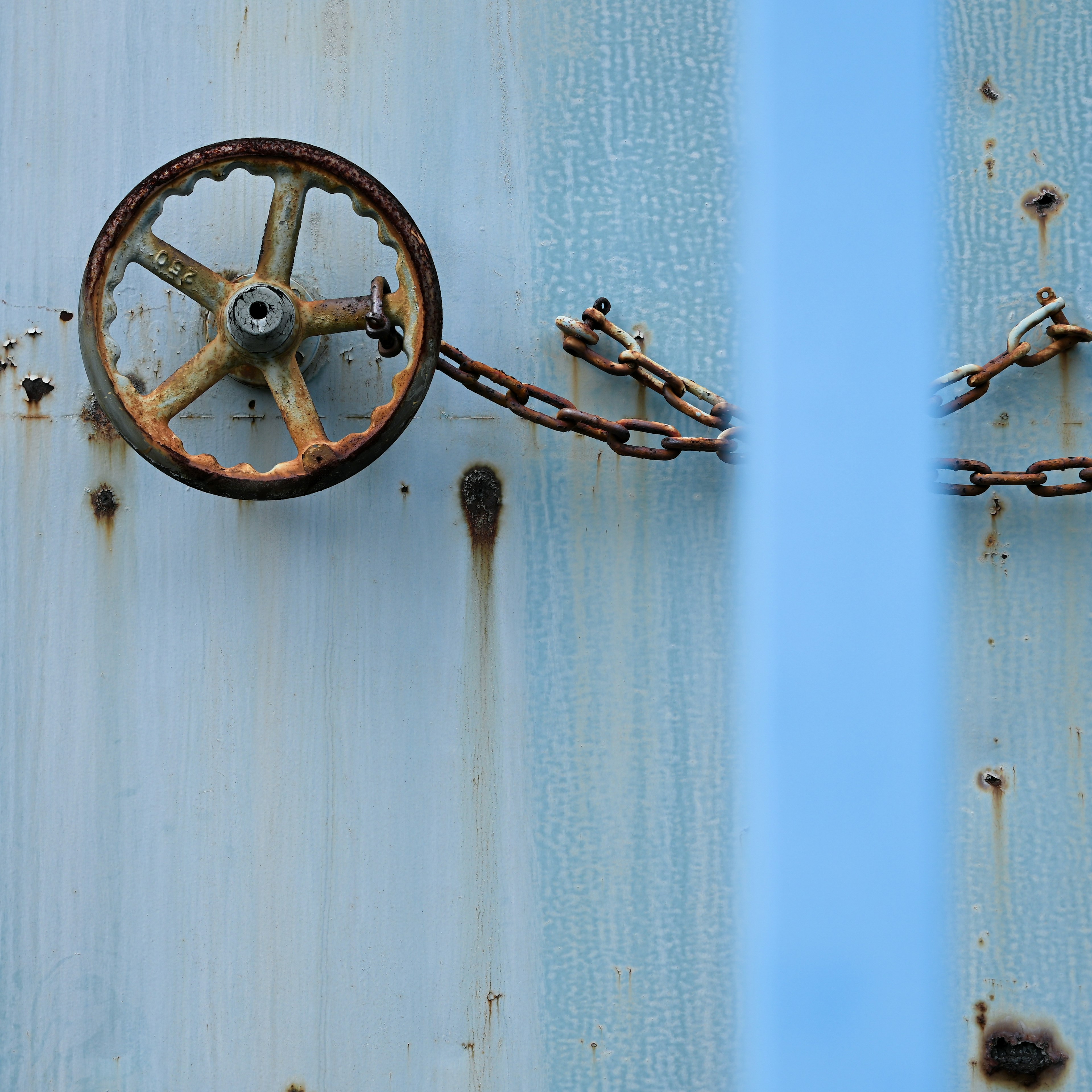 Roues rouillées et chaîne sur un mur en métal bleu