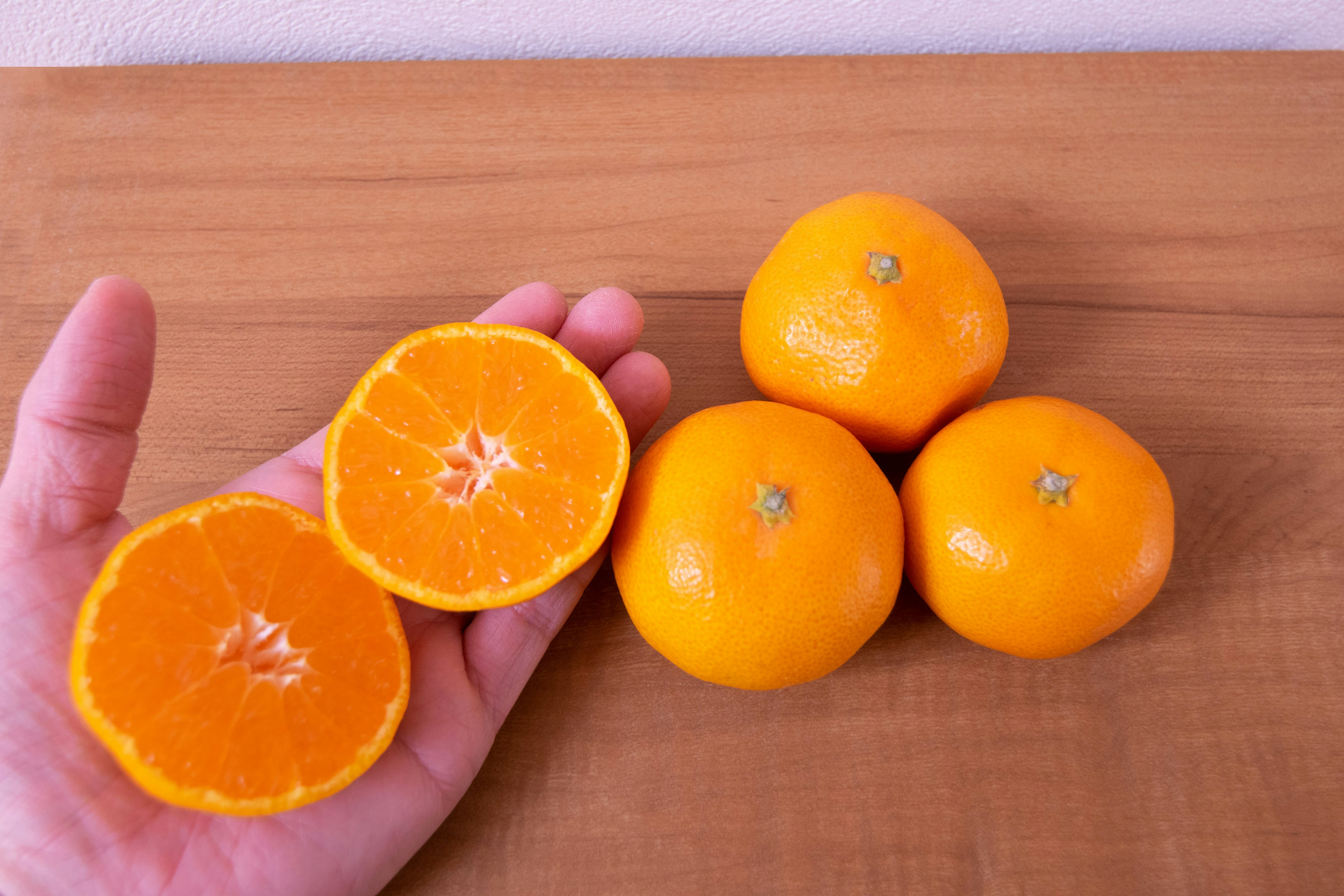 A hand holding a halved orange with whole oranges arranged nearby