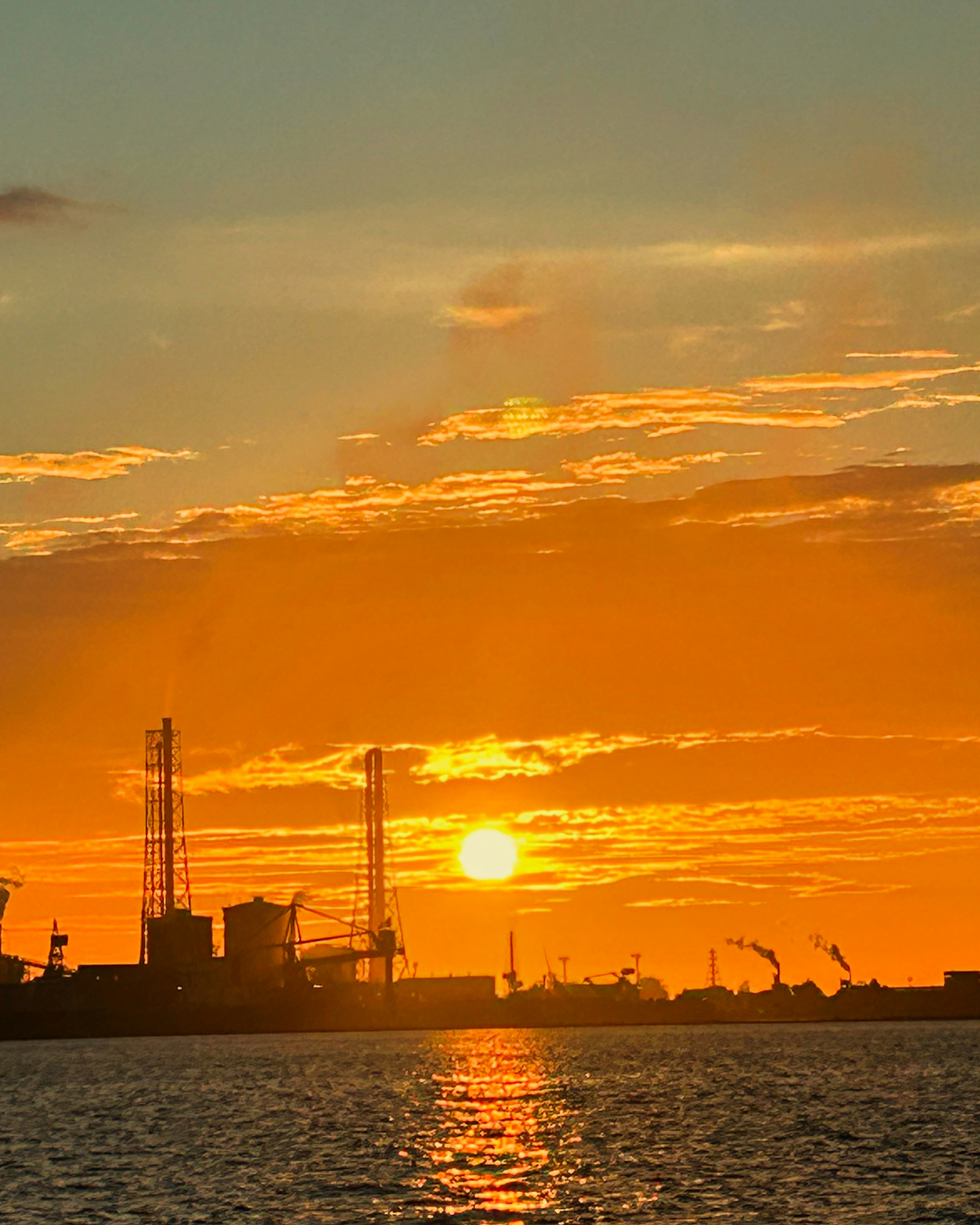 Sonnenuntergang über einer Industrieanlage mit Silhouetten von Kränen