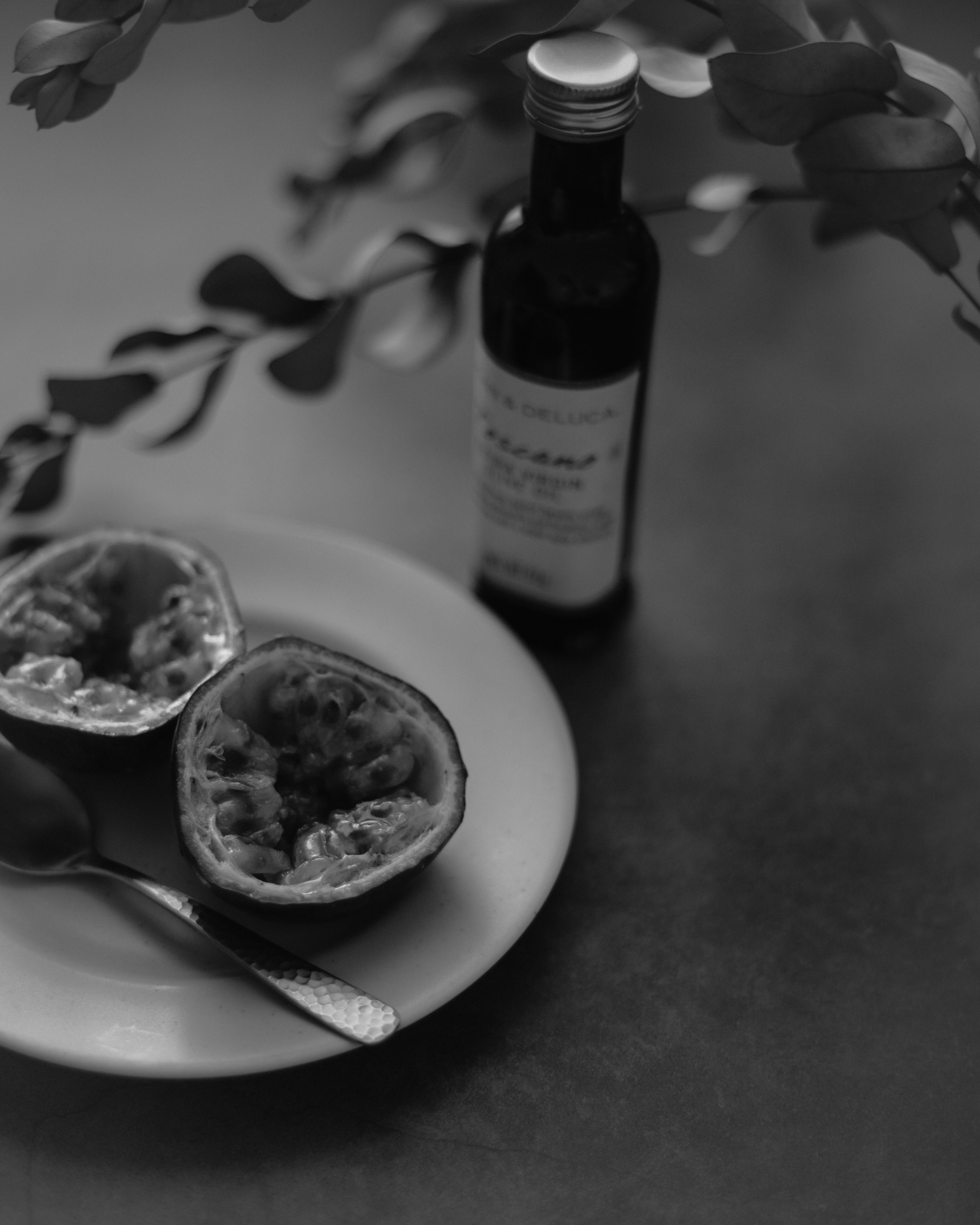 A plate with halved passion fruit and a spoon alongside a bottle in black and white