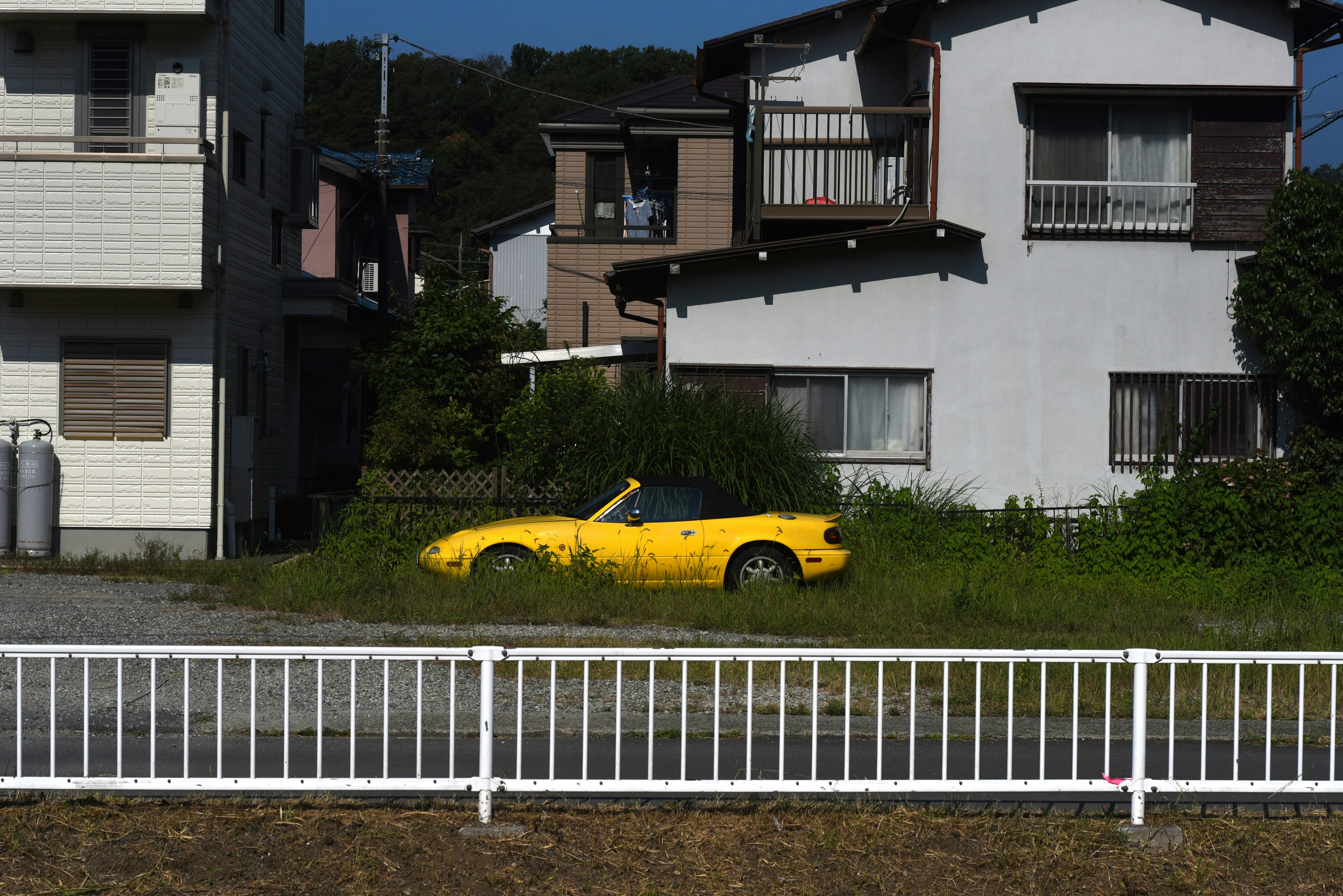 Ein gelbes Cabrio, das in einem grasbewachsenen Bereich neben Häusern geparkt ist