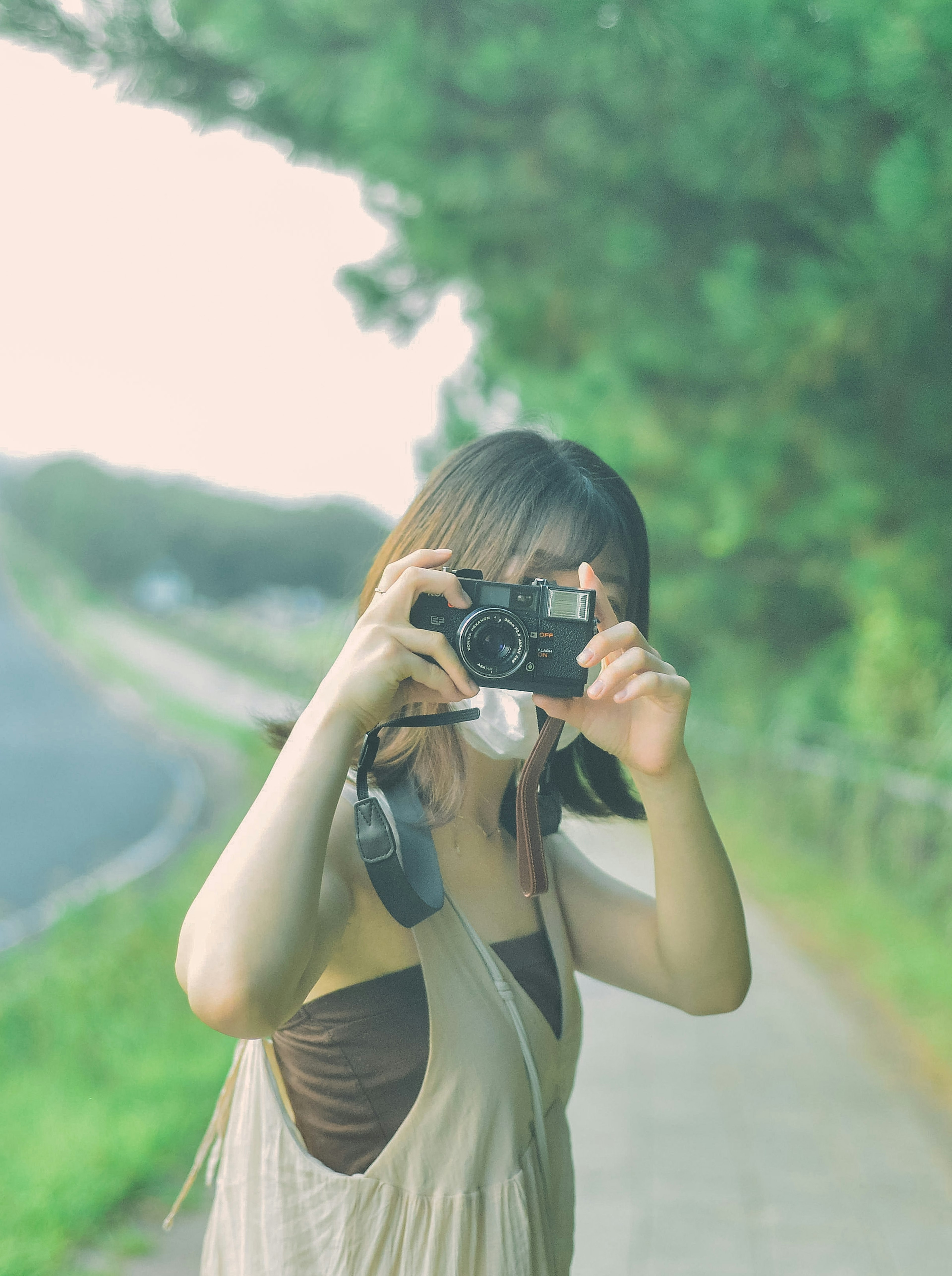 A woman holding a camera on a path with greenery in the background