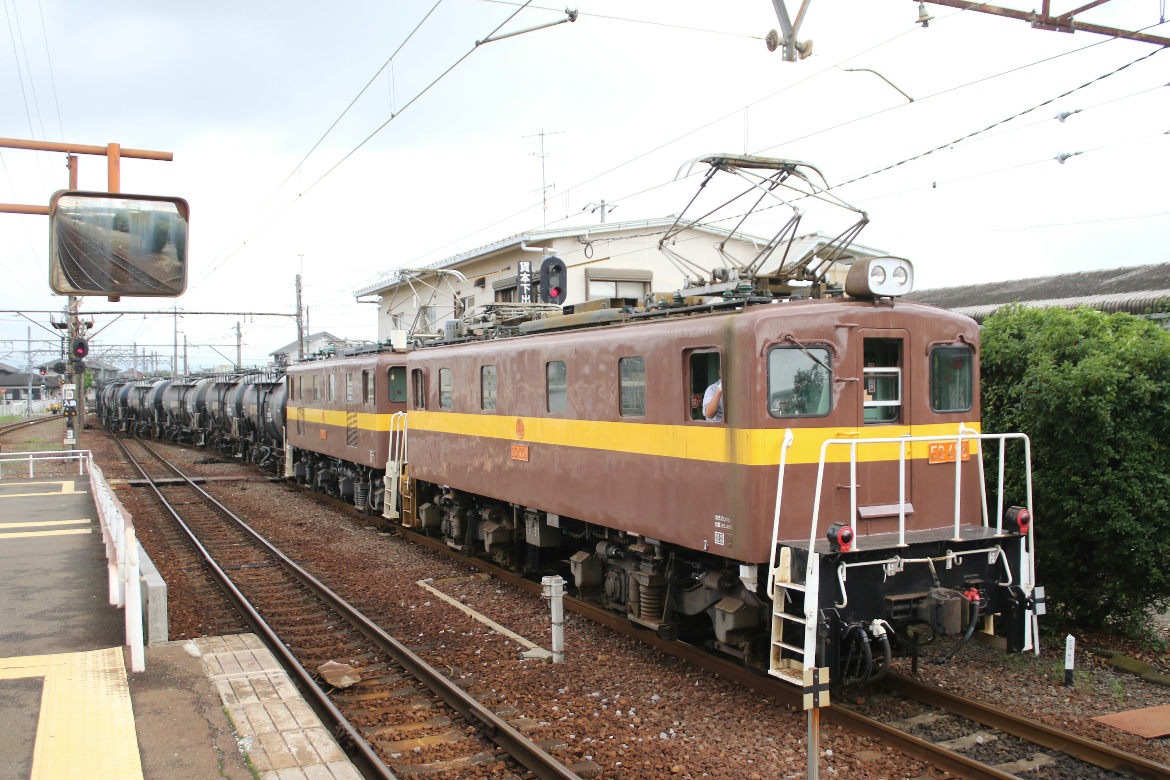 Brown electric locomotive pulling multiple freight cars at a station