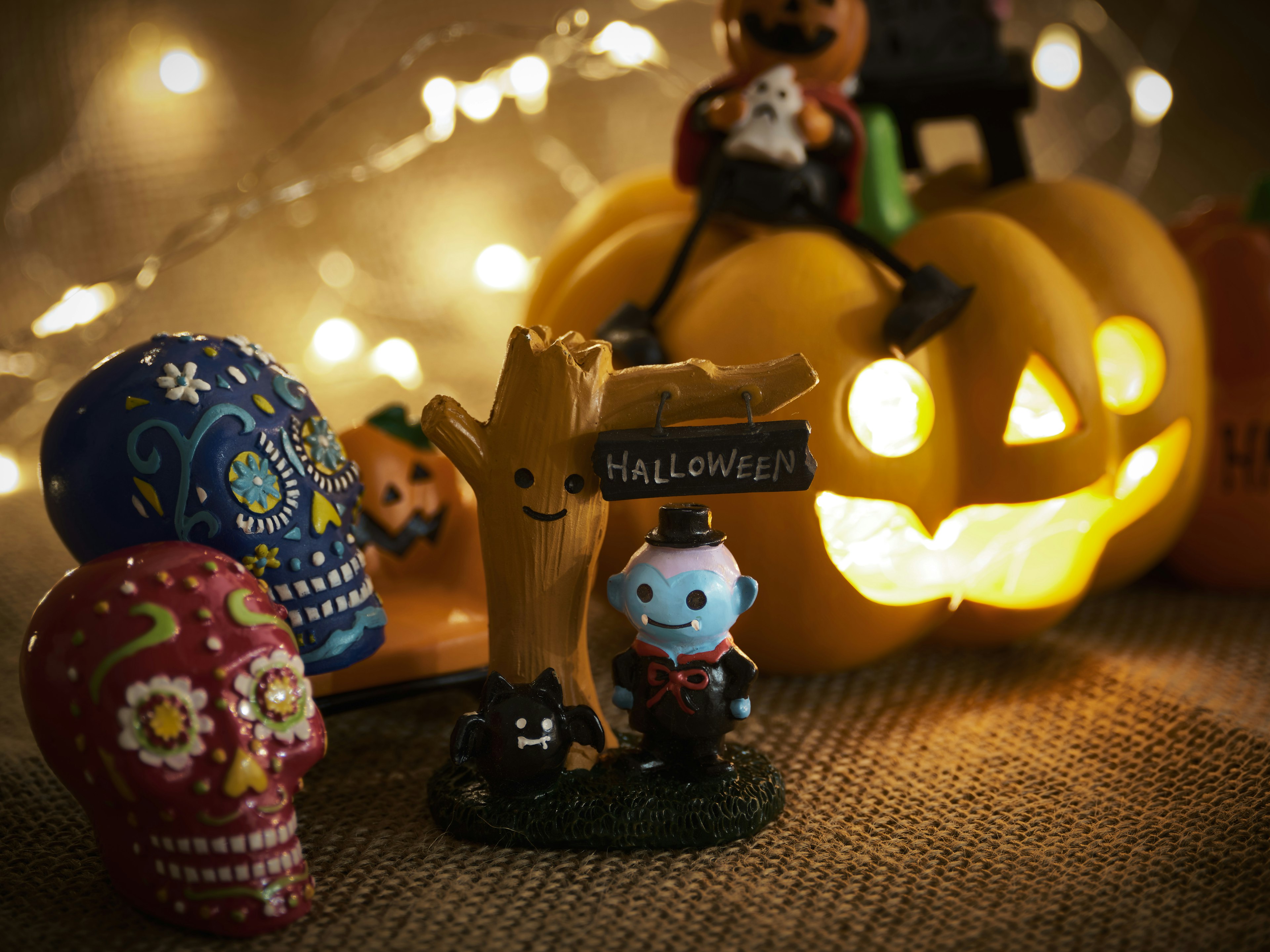 A festive Halloween display featuring colorful skull figurines and a pumpkin with a lit face