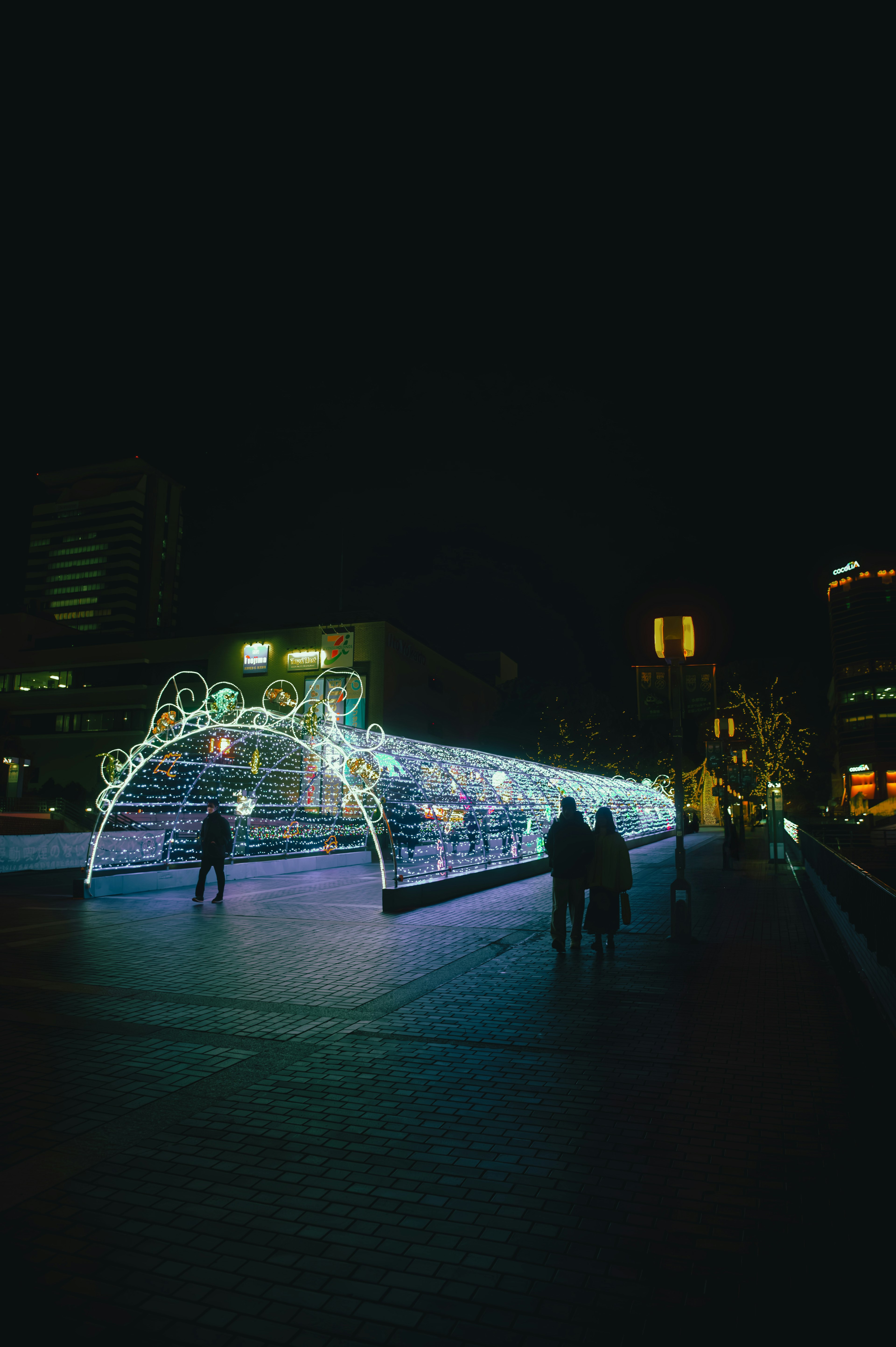 Illuminated archway at night with silhouettes of people