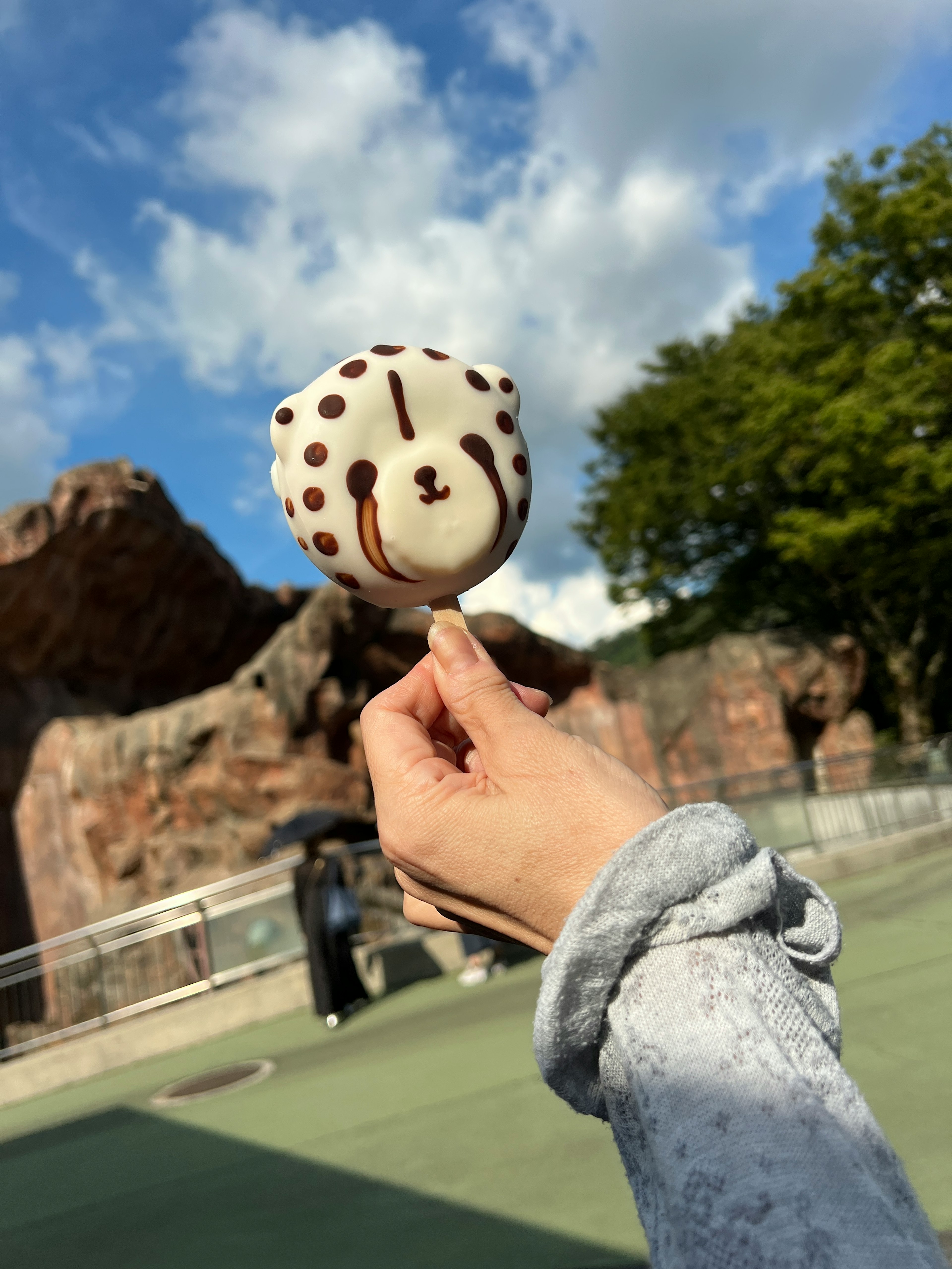 Eine bärchenförmige Süßigkeit in der Hand gehalten mit blauem Himmel und grünen Bäumen im Hintergrund