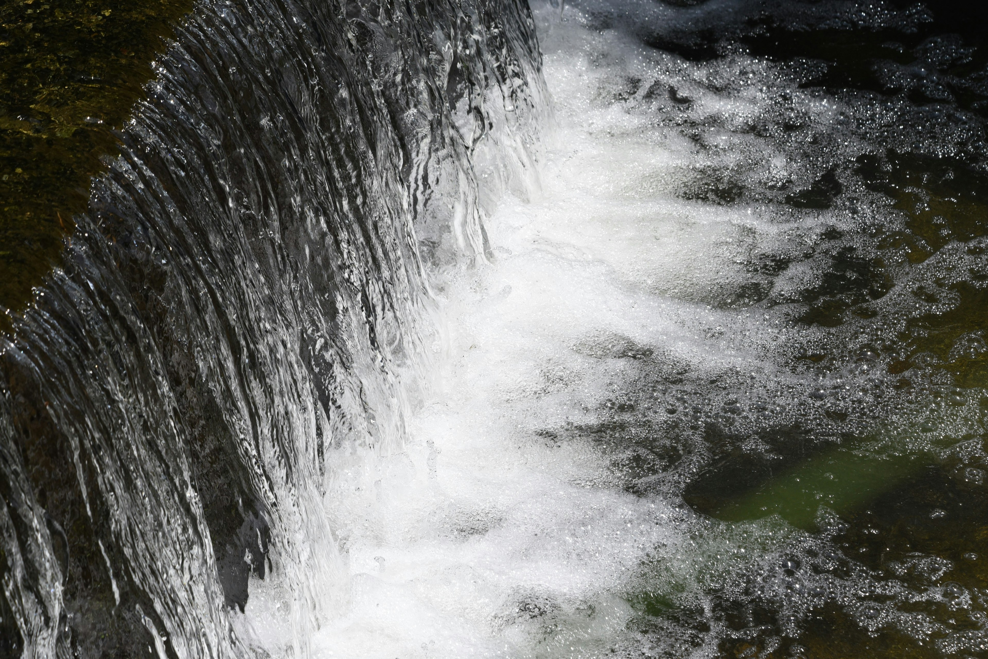 Cascata d'acqua con schiuma bianca che scorre su rocce superficie d'acqua verde