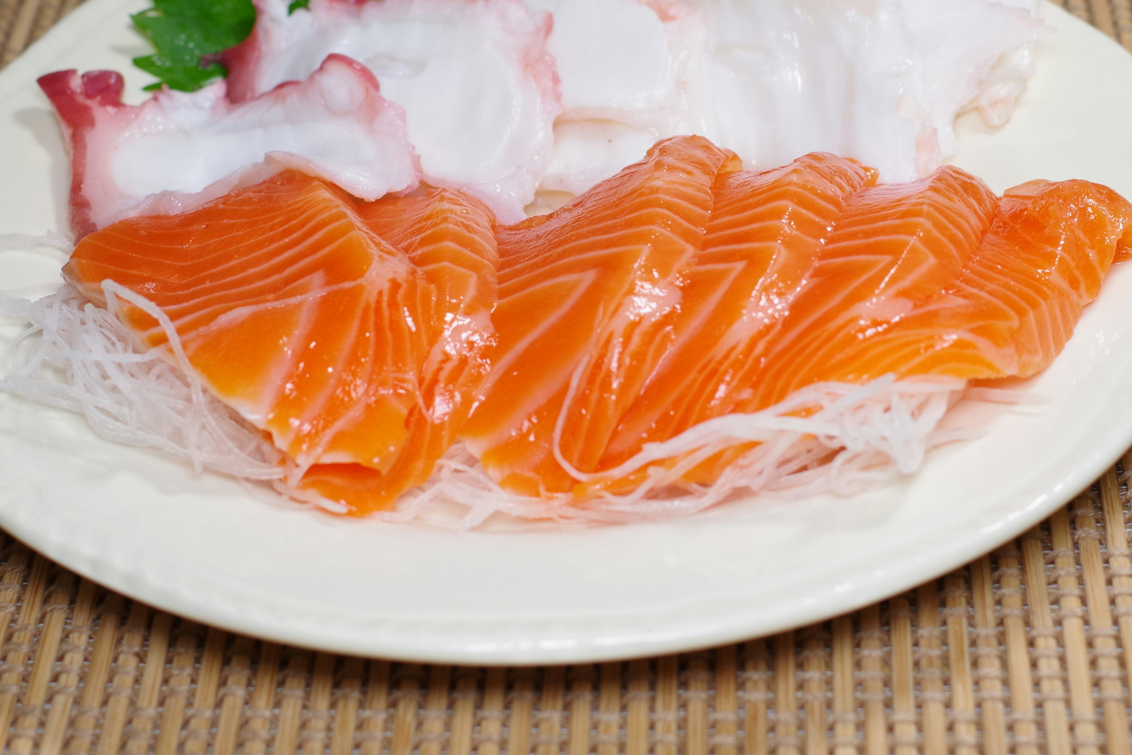 Sashimi salmon oranye cerah dan sashimi cumi putih disajikan di atas piring