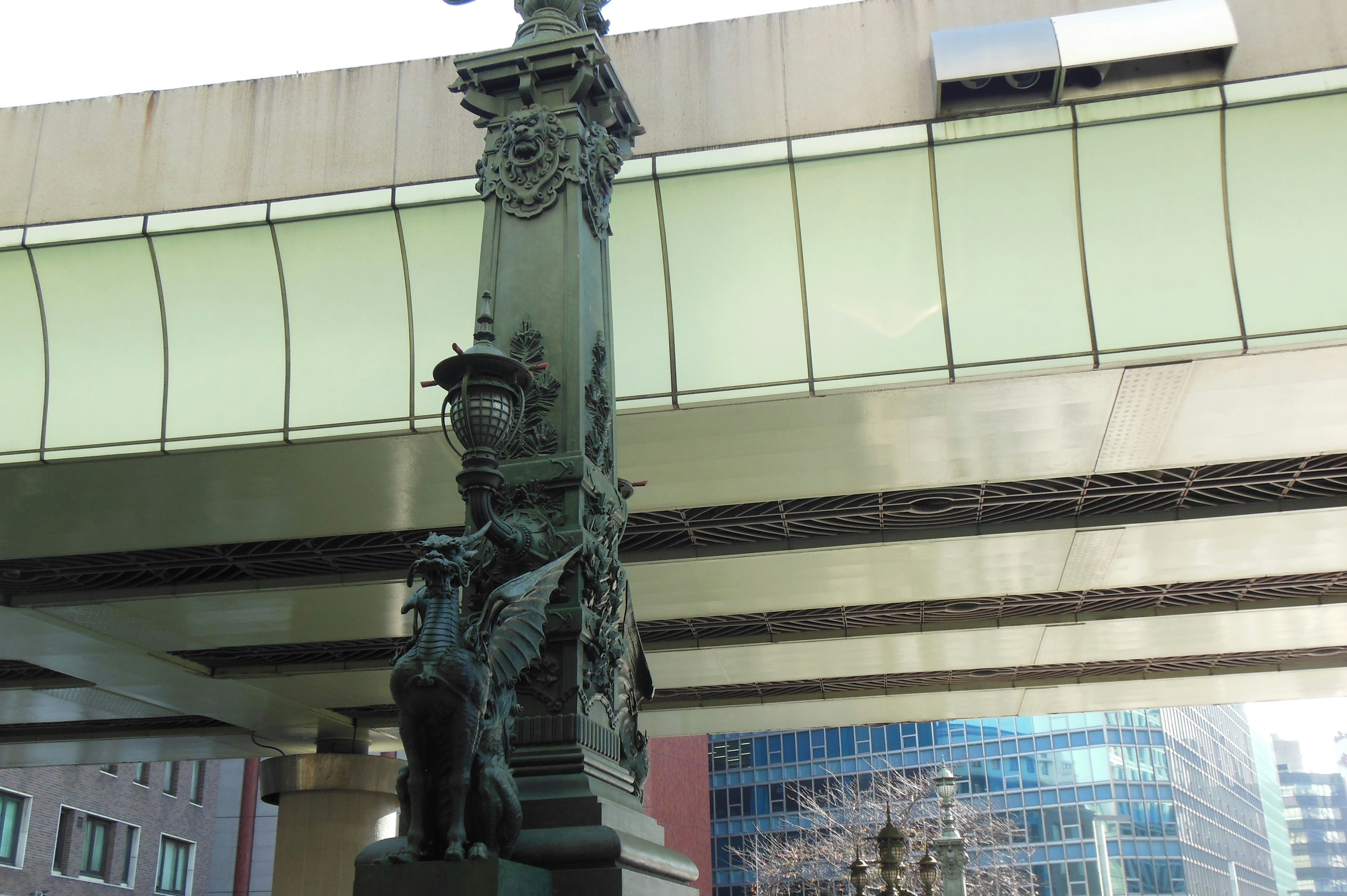 Decorative column under a bridge with modern buildings in the background