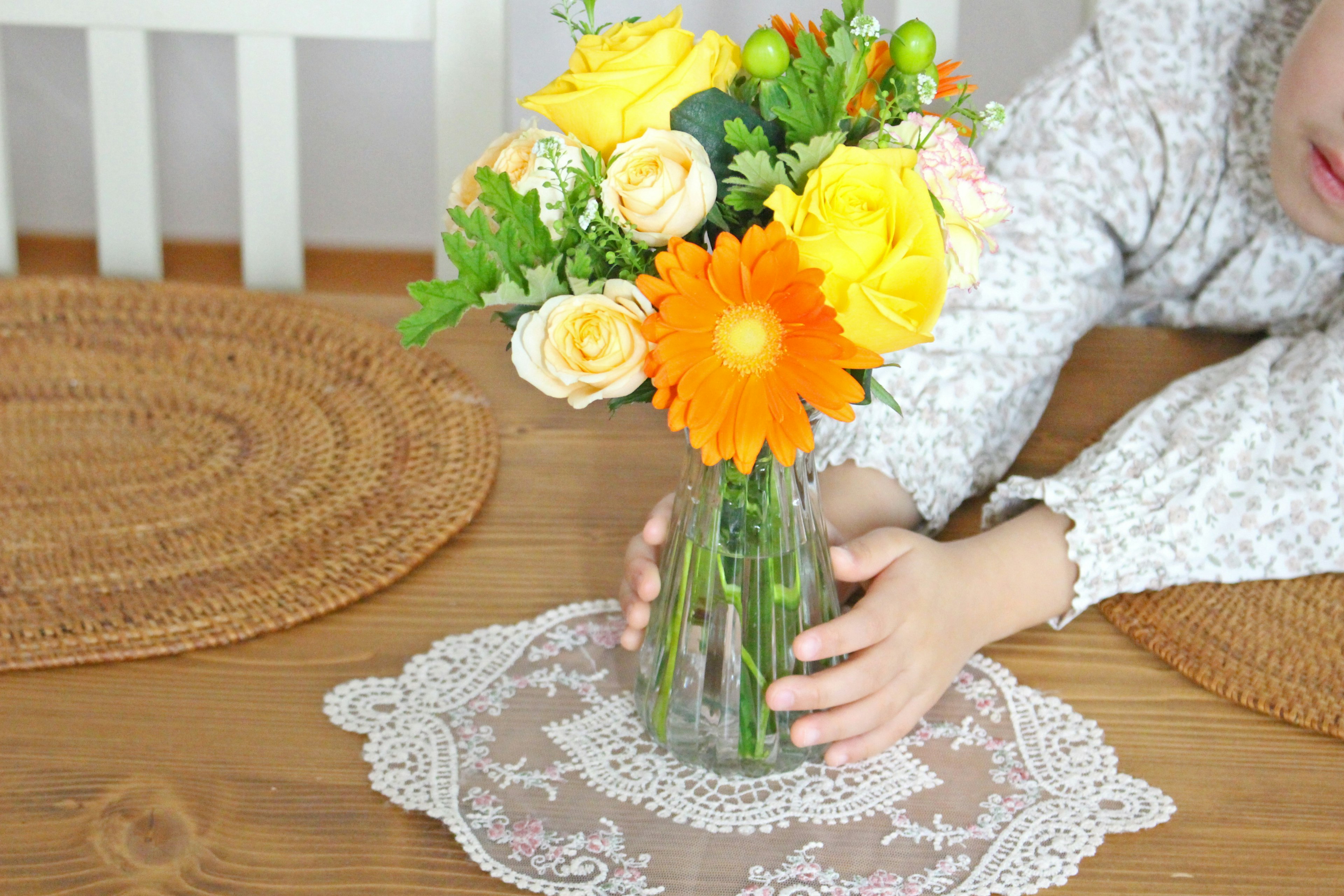 Child placing a colorful flower bouquet on a lace table runner