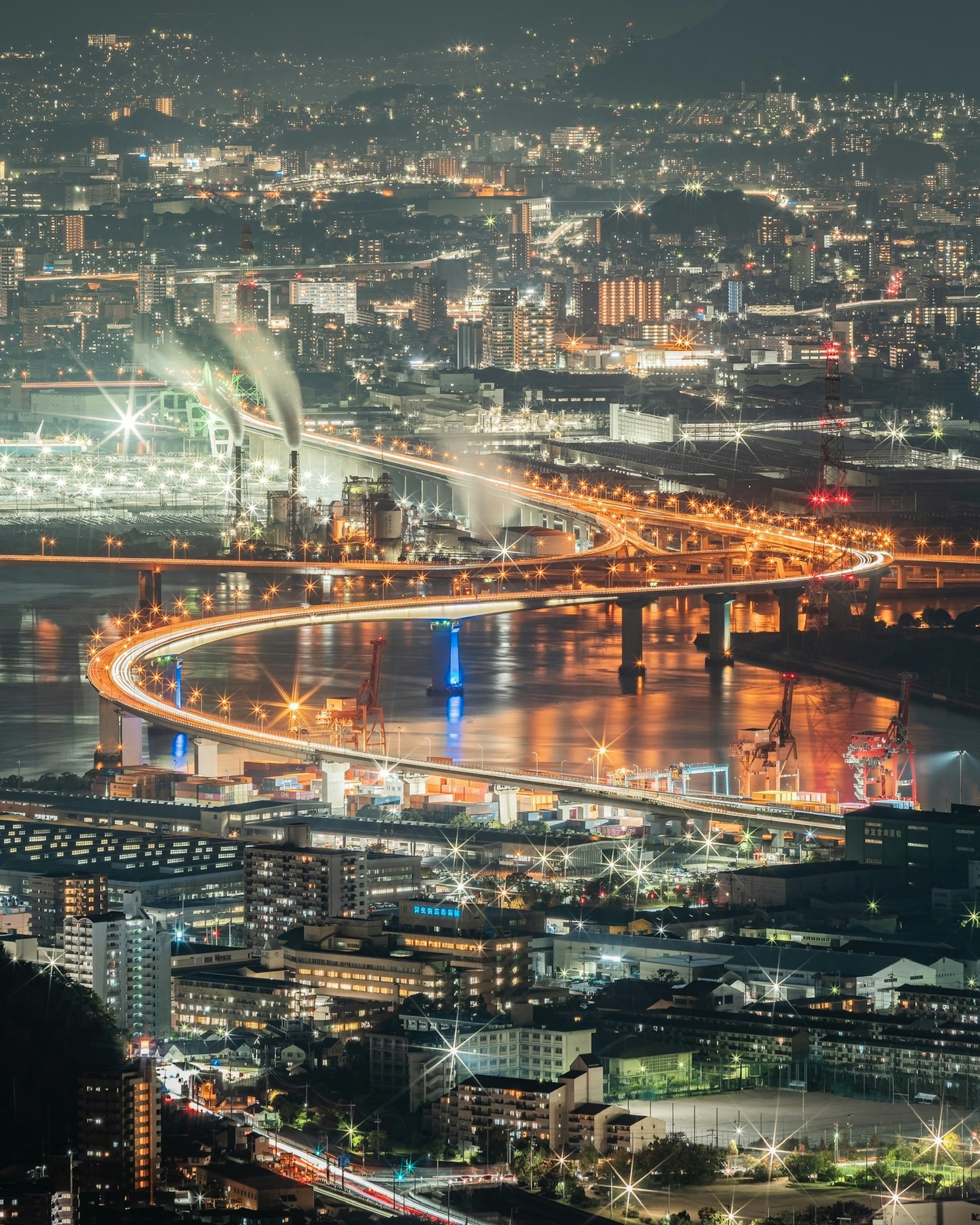 Night view of a cityscape featuring a winding bridge and bright lights