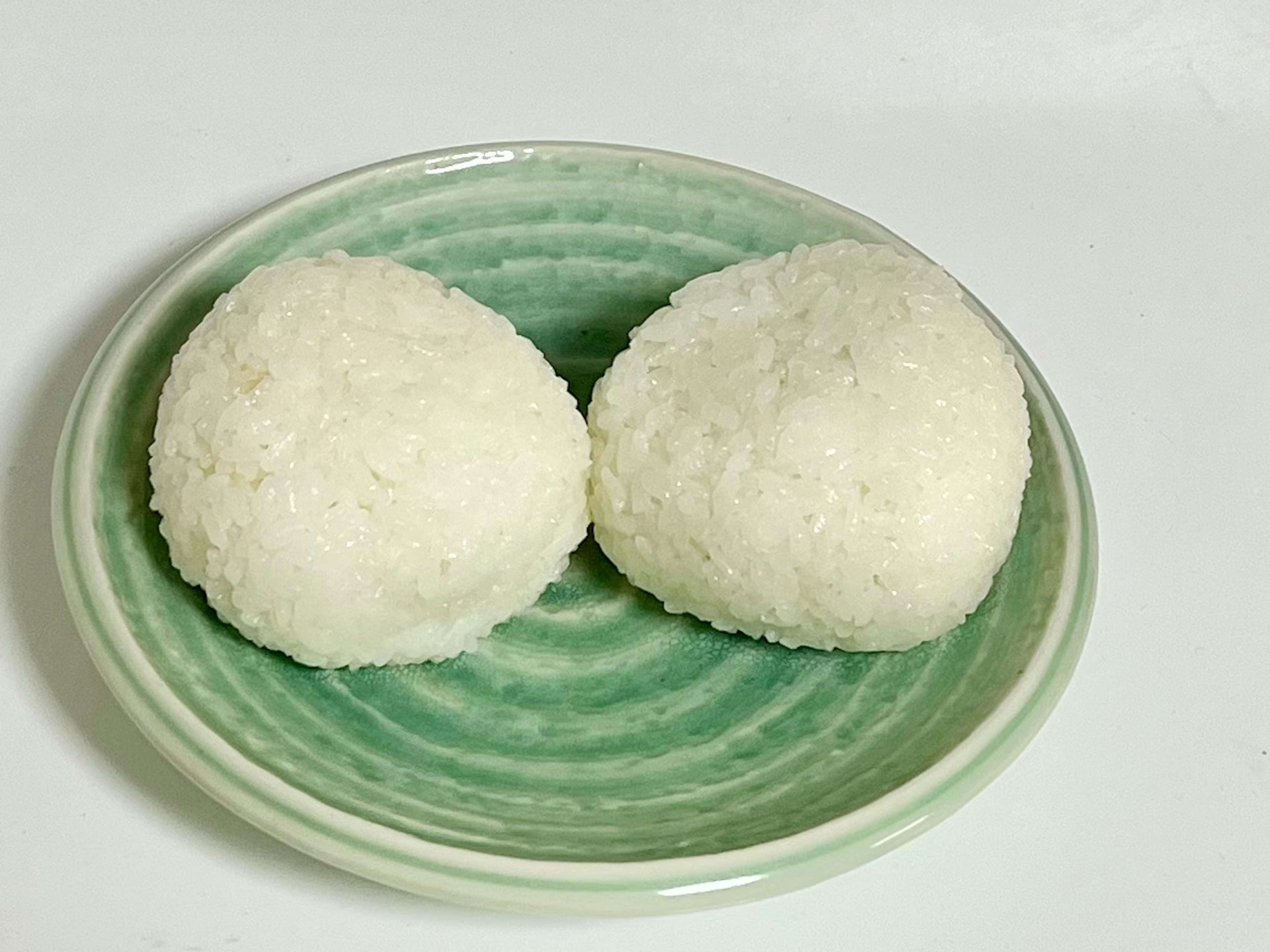 Two white rice balls on a green plate