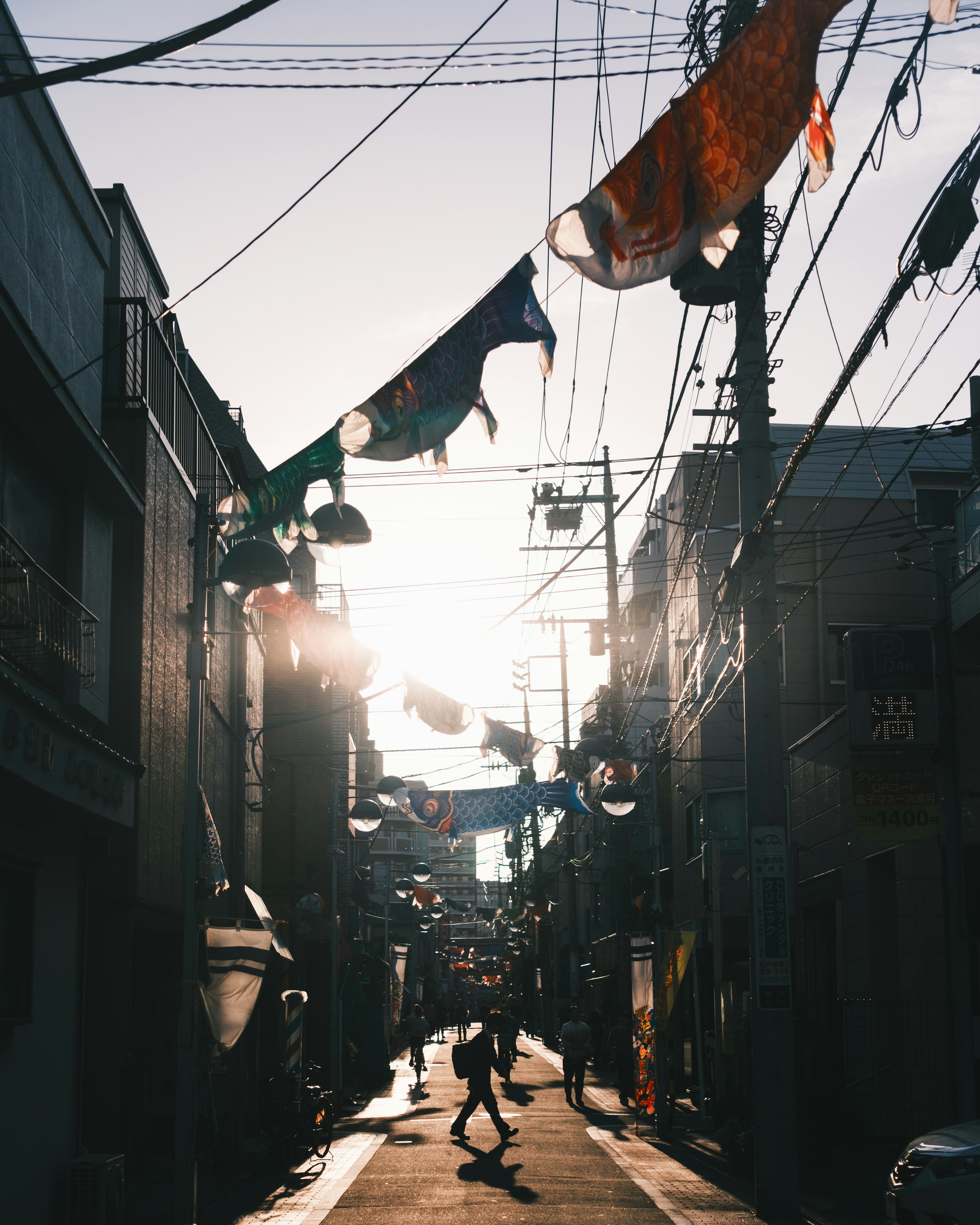 People walking in a narrow alley with sunlight shining through colorful fabric banners