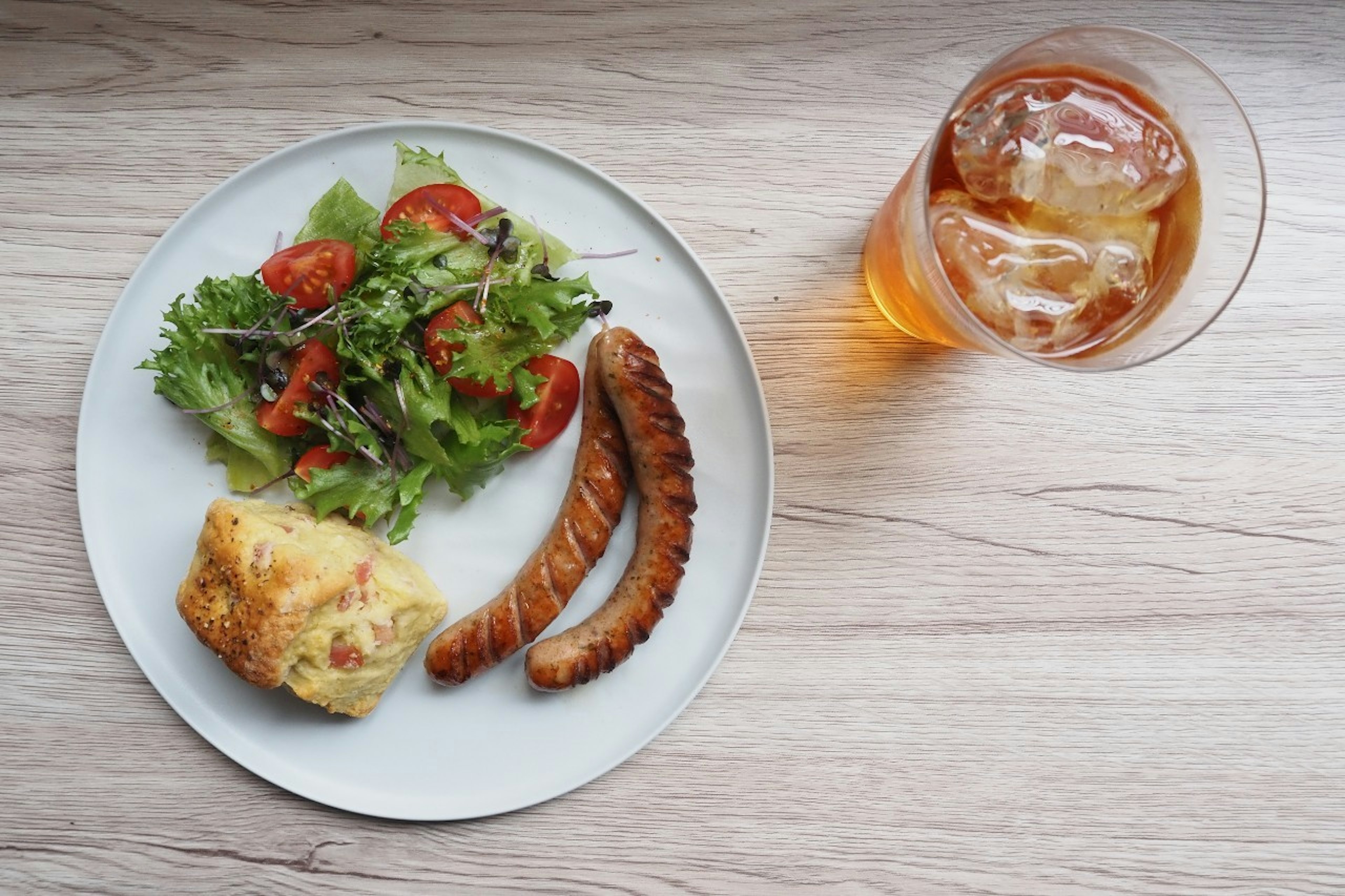 Eine Mahlzeit mit einem Salat mit Tomaten, zwei Würstchen, einem Omelett und Eistee