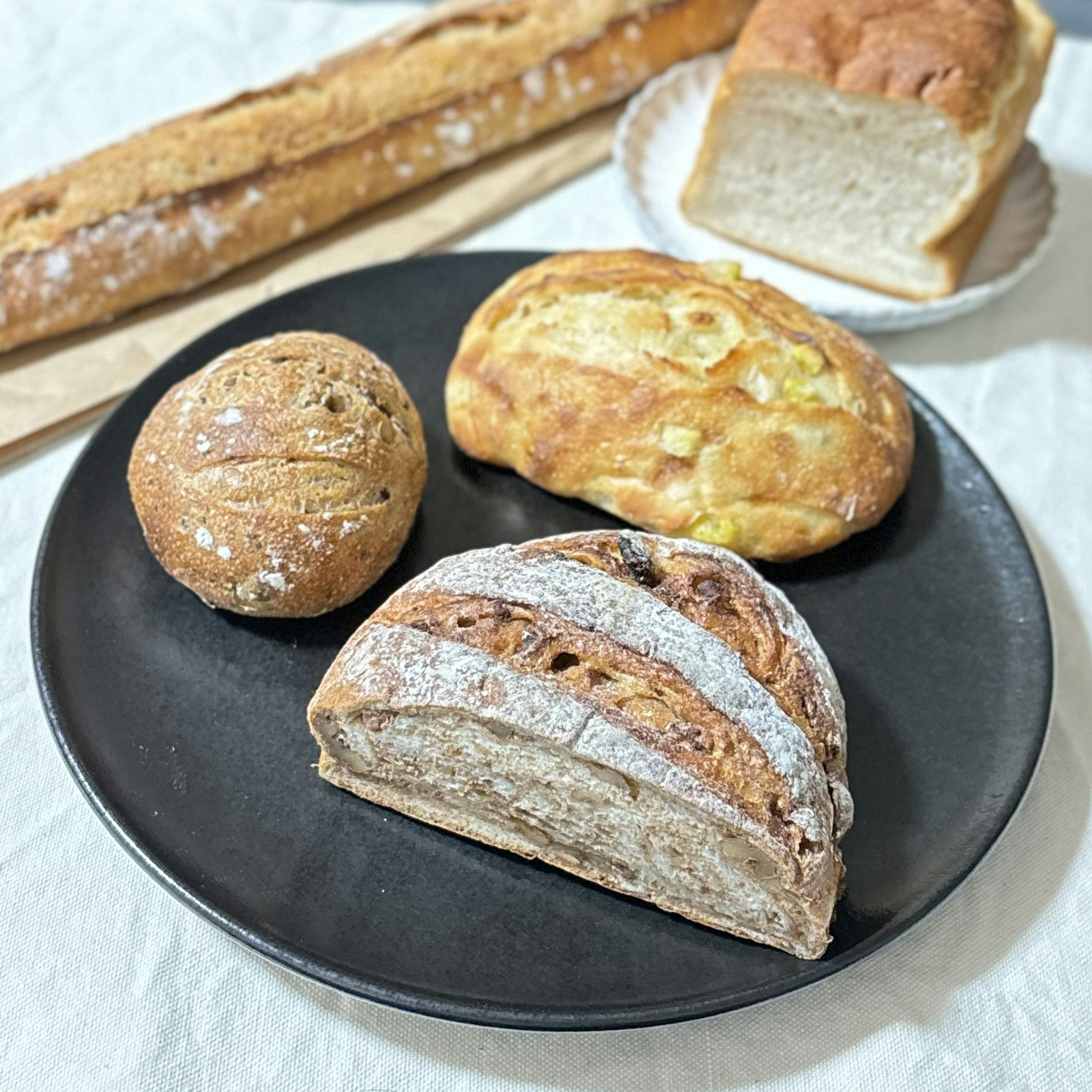 Verschiedene Brotsorten auf einem schwarzen Teller mit einem Baguette im Hintergrund