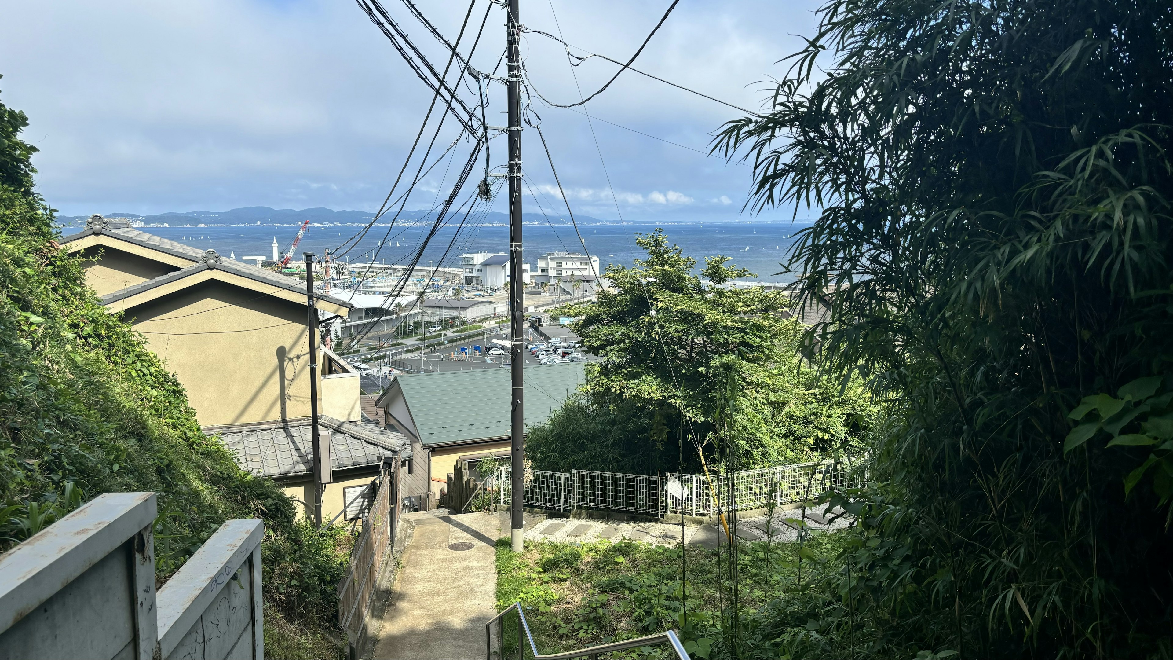 Scenic view of a sloped road overlooking the sea and town with power lines