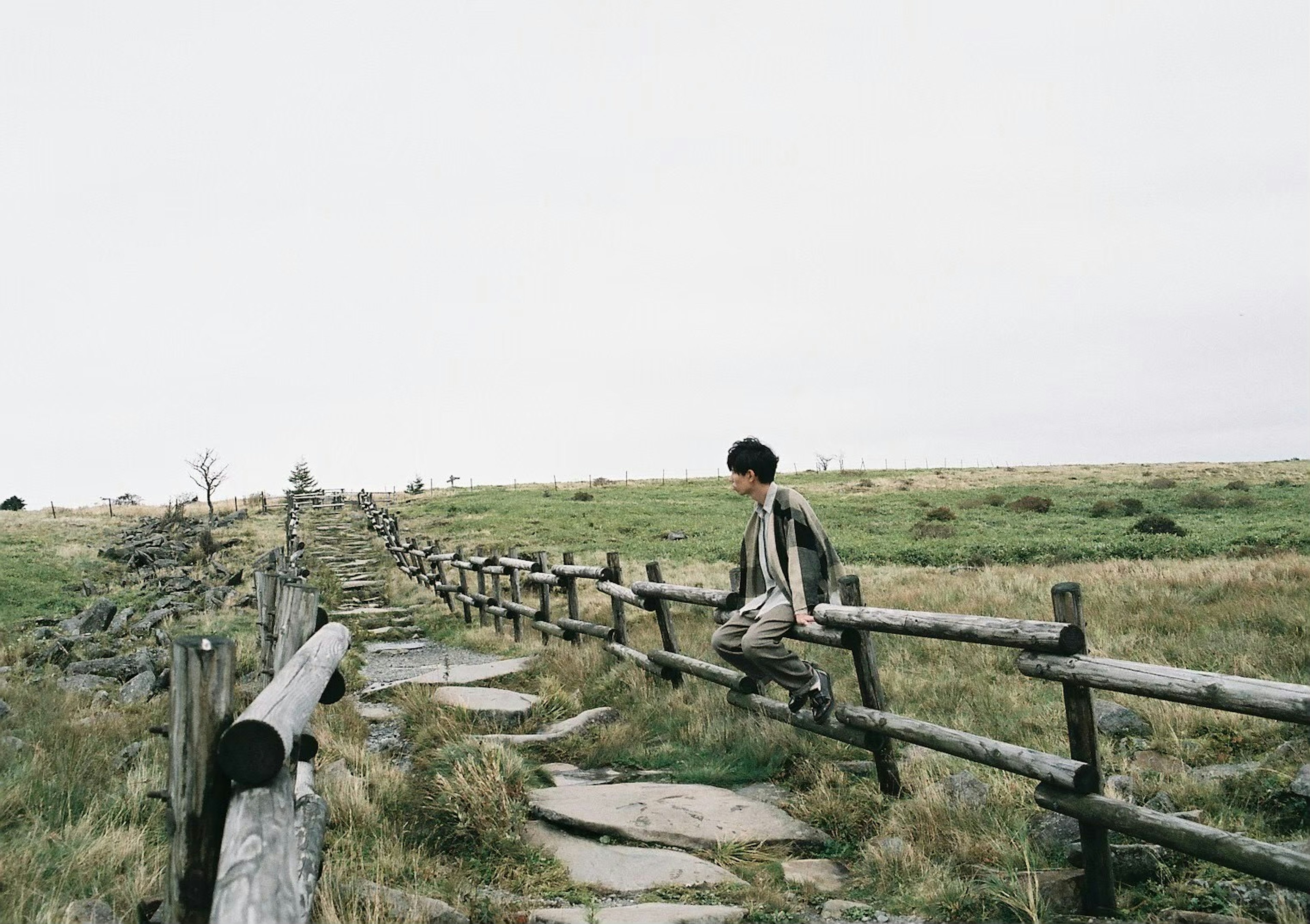 Person sitting on a wooden fence along a grassy path