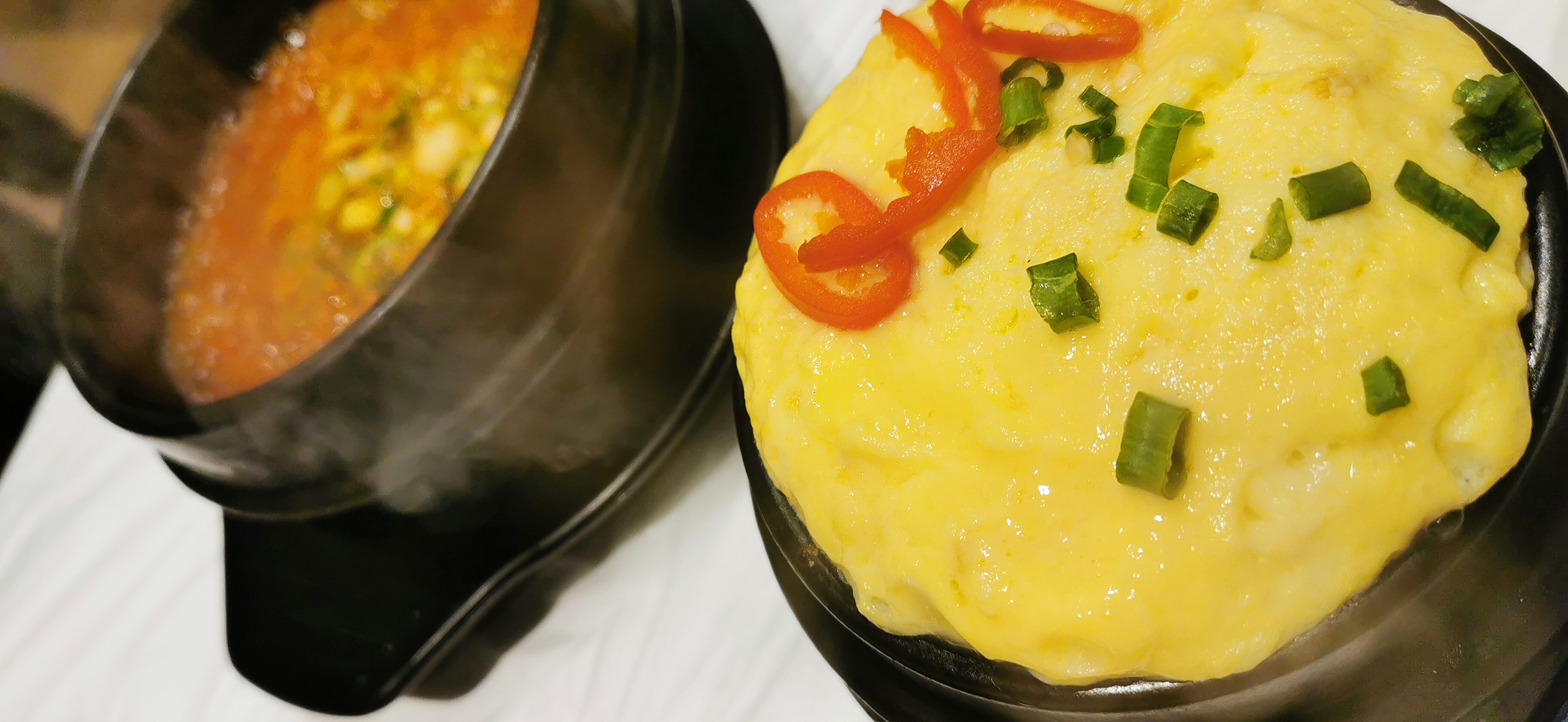 A bowl of soup alongside a fluffy egg dish garnished with red chili and green onions