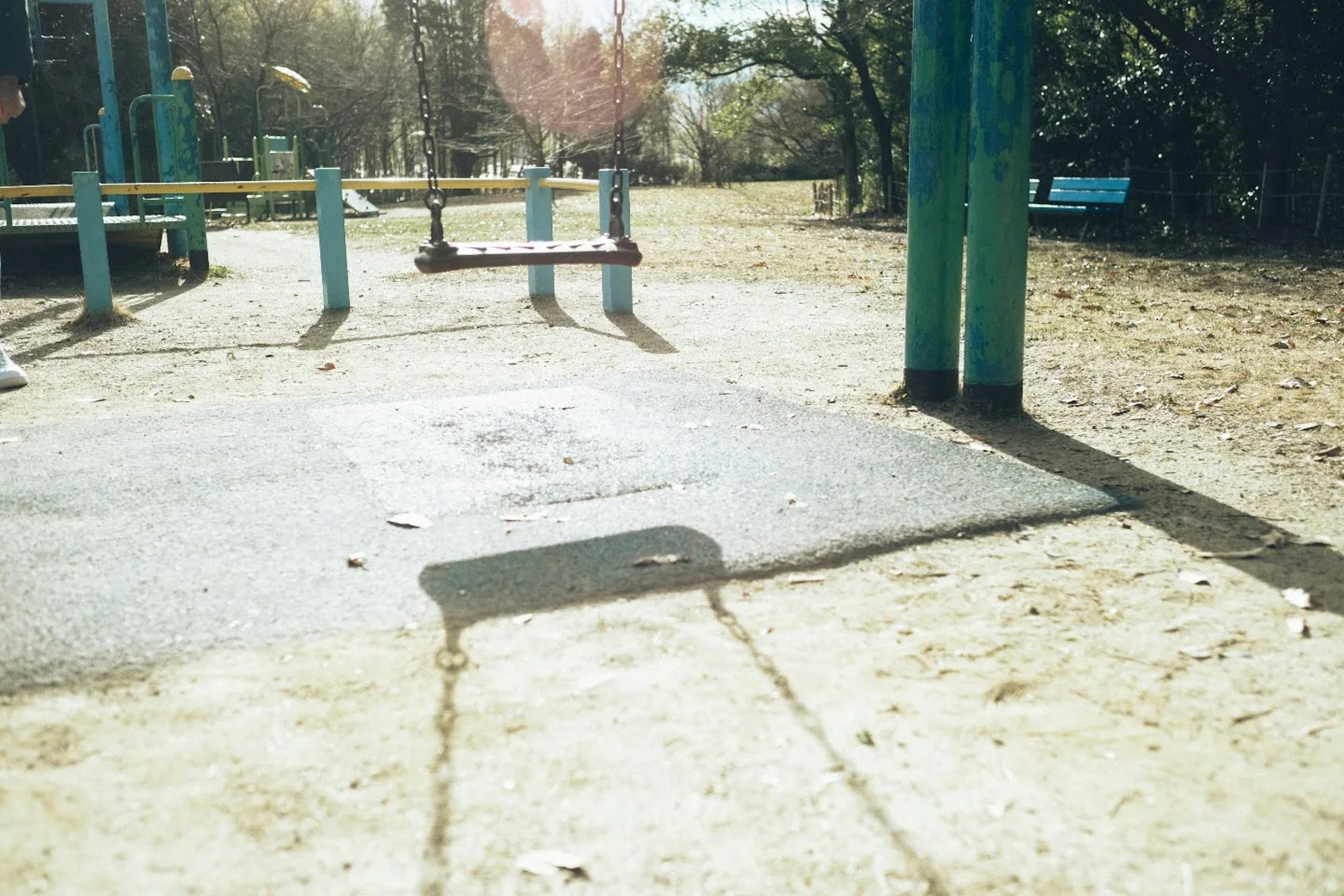 Blick auf eine Parkschaukel mit blauen Stützen und sandigem Boden