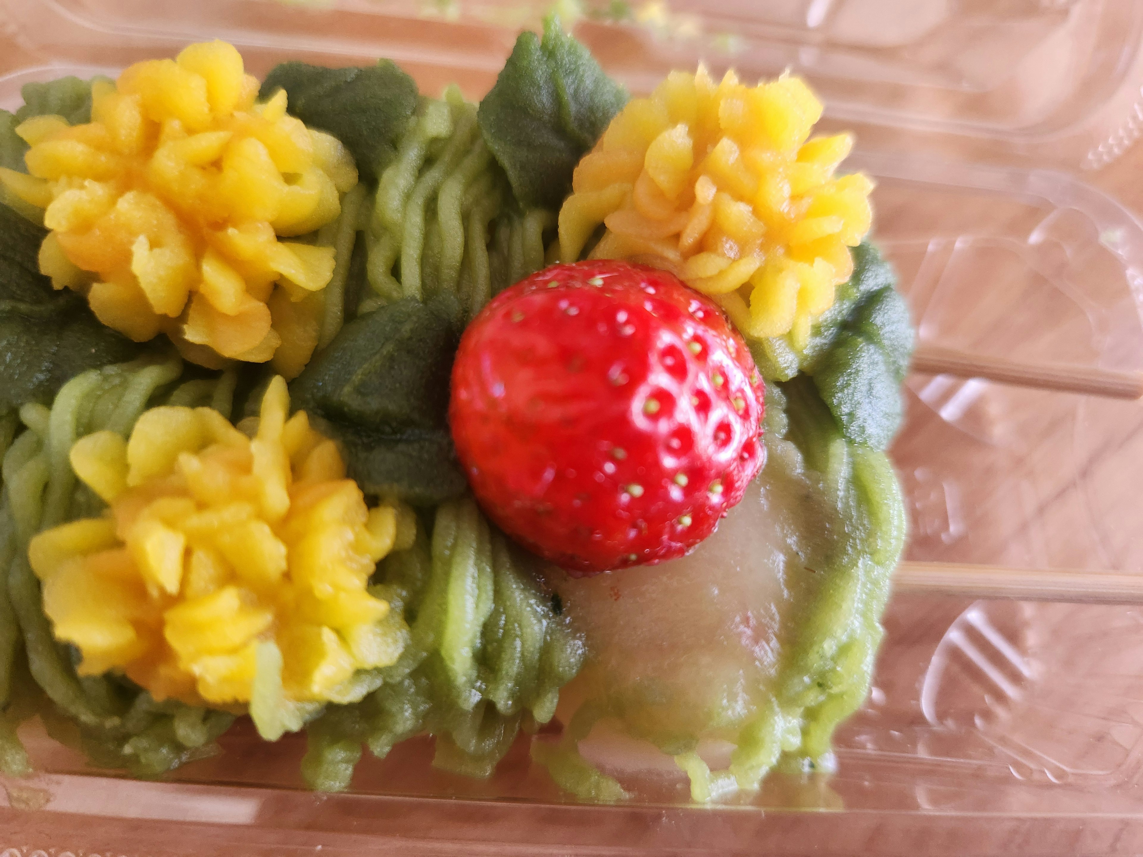 Green dessert topped with yellow flowers and a red strawberry