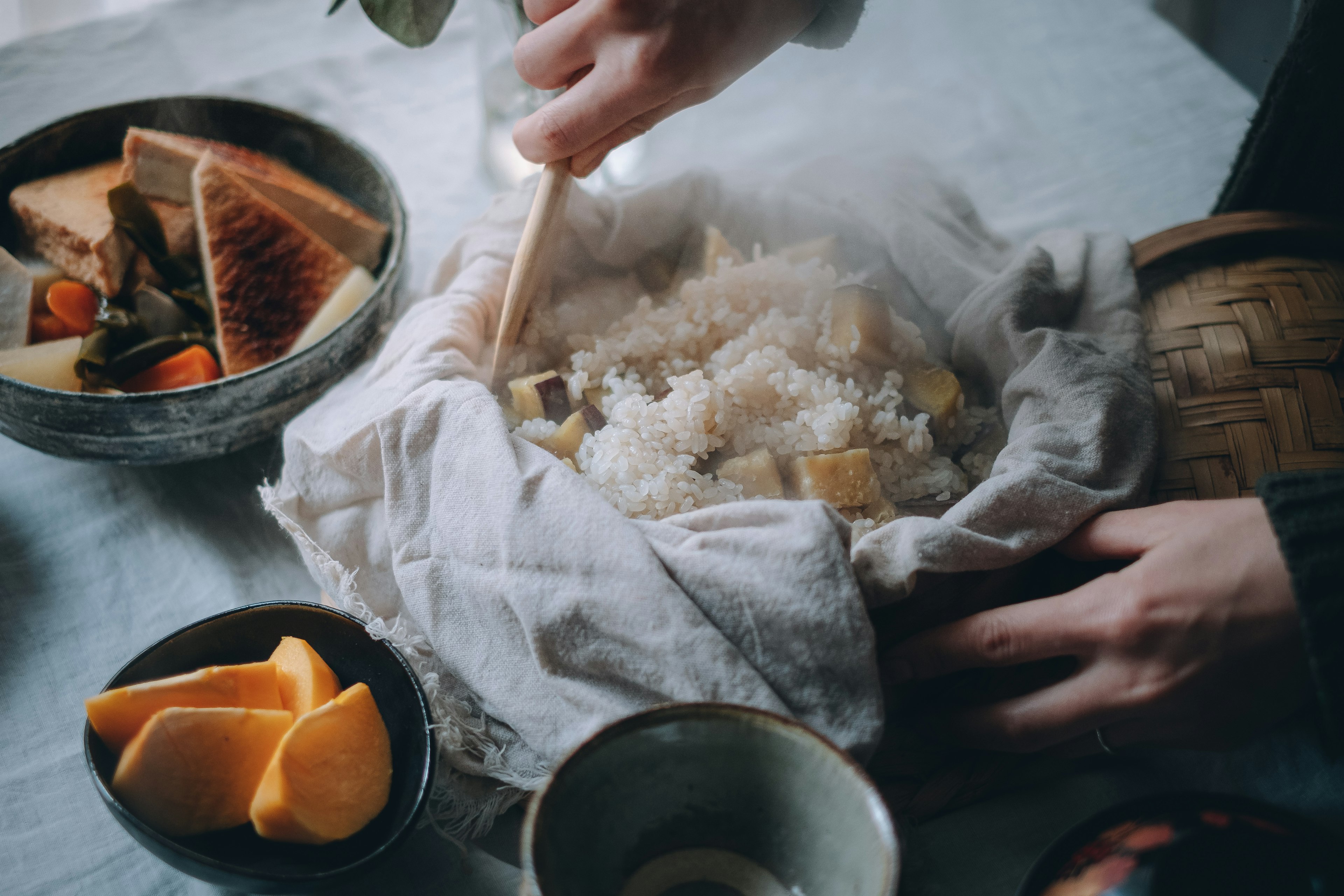 Person stirring fluffy rice in a cloth with warm dishes and fruit on the table