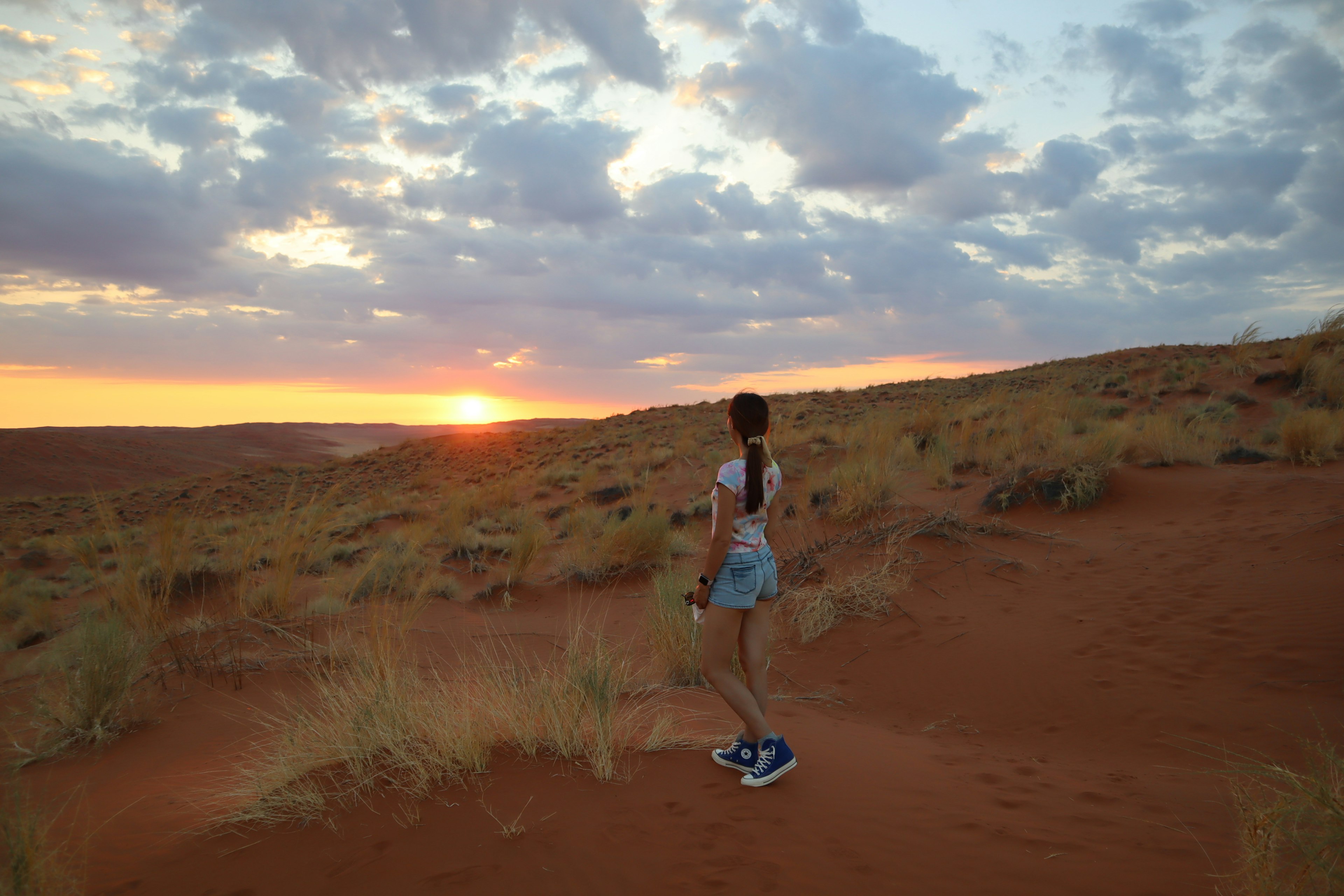 Silhouette einer Frau, die auf Sanddünen mit Sonnenuntergang im Hintergrund geht