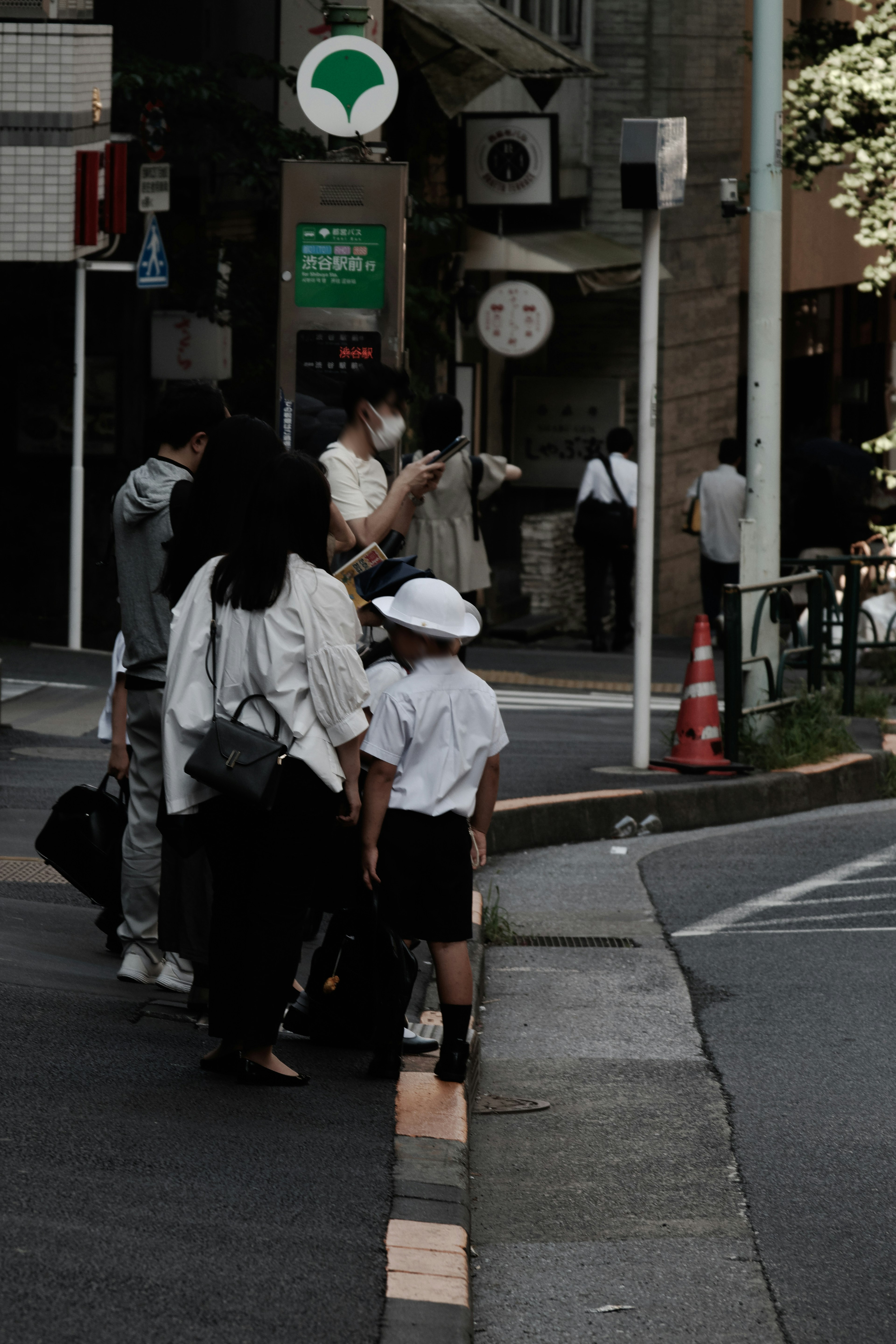 People waiting at a crosswalk a small child wearing a white hat