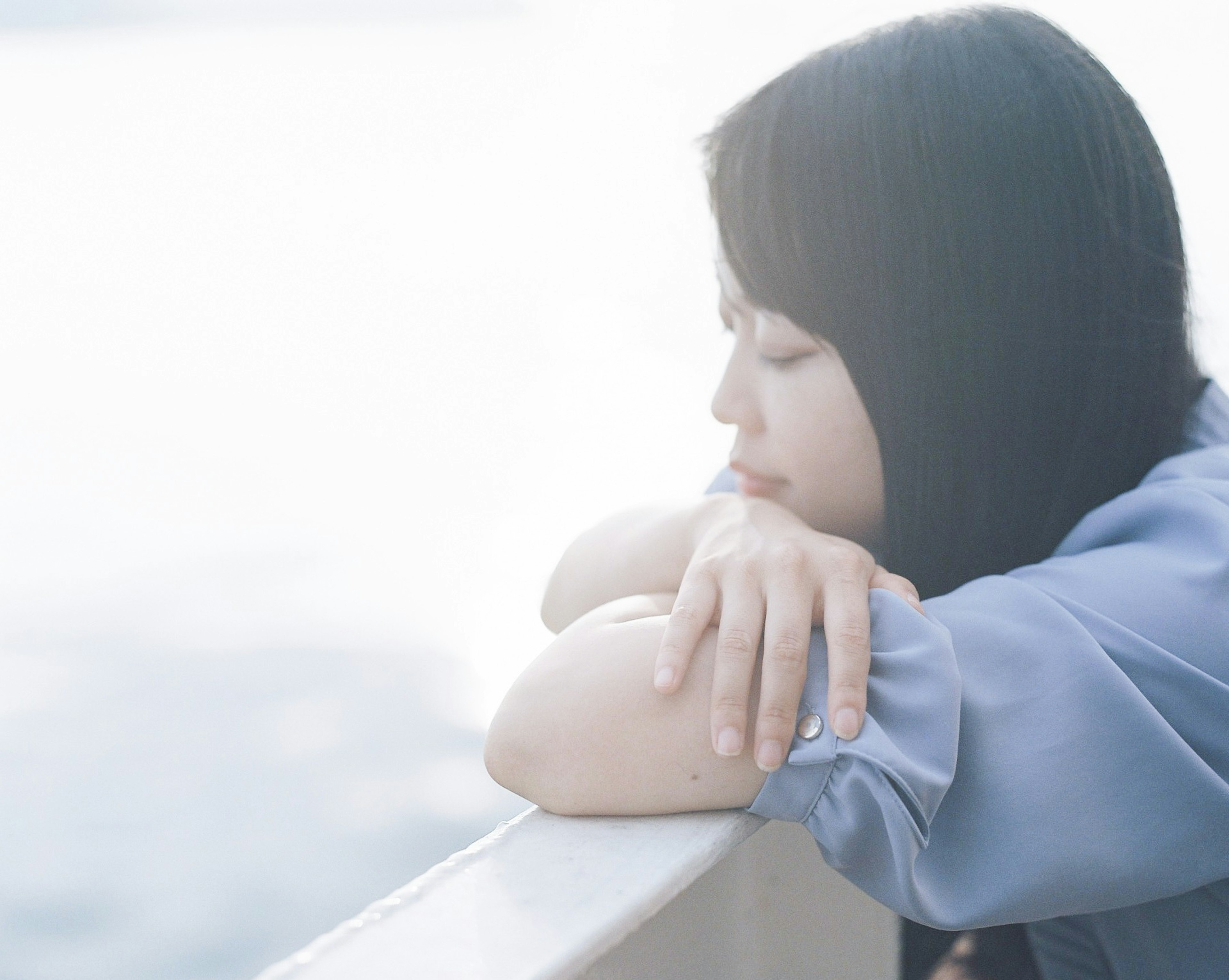 A woman resting her arms on a boat railing gazing at the calm sea