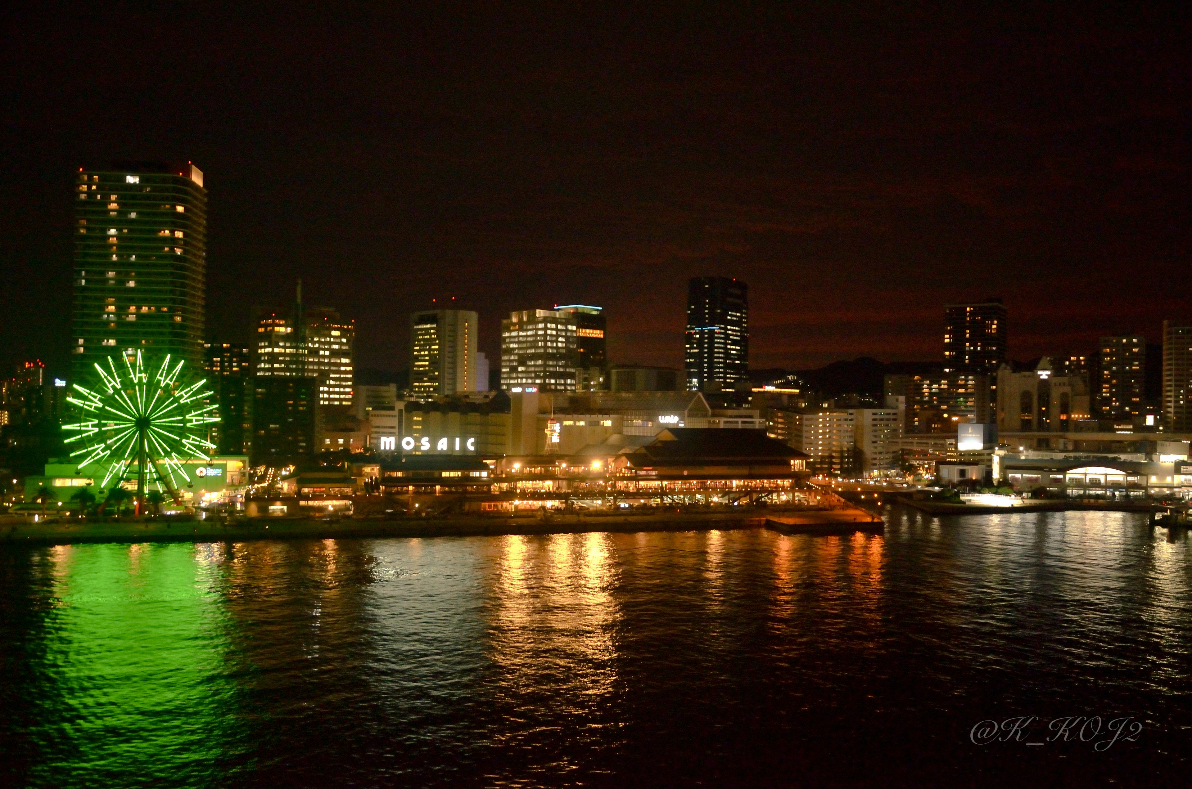 夜间城市景观，绿色摩天轮和灯光闪烁的建筑