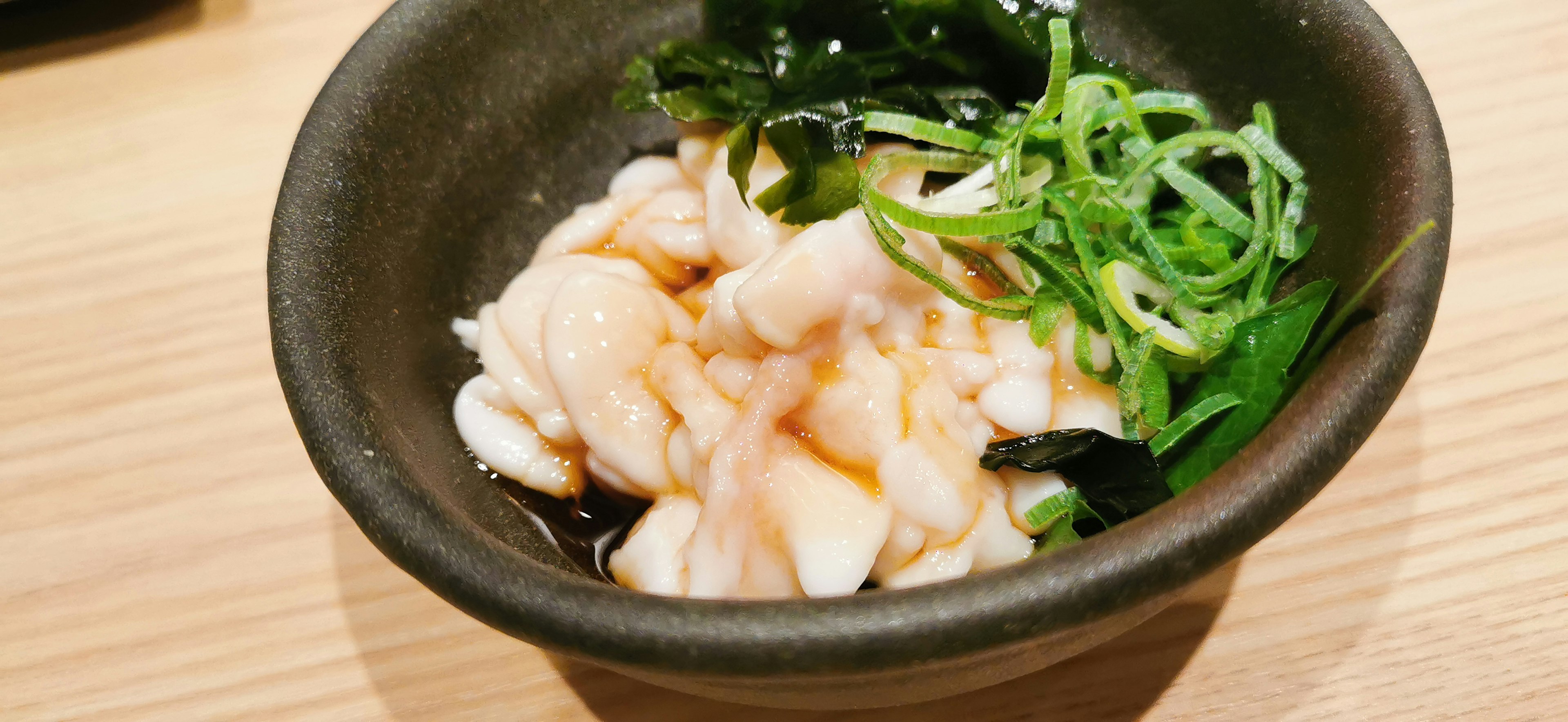 Japanese dish served in a black bowl topped with seaweed and green onions