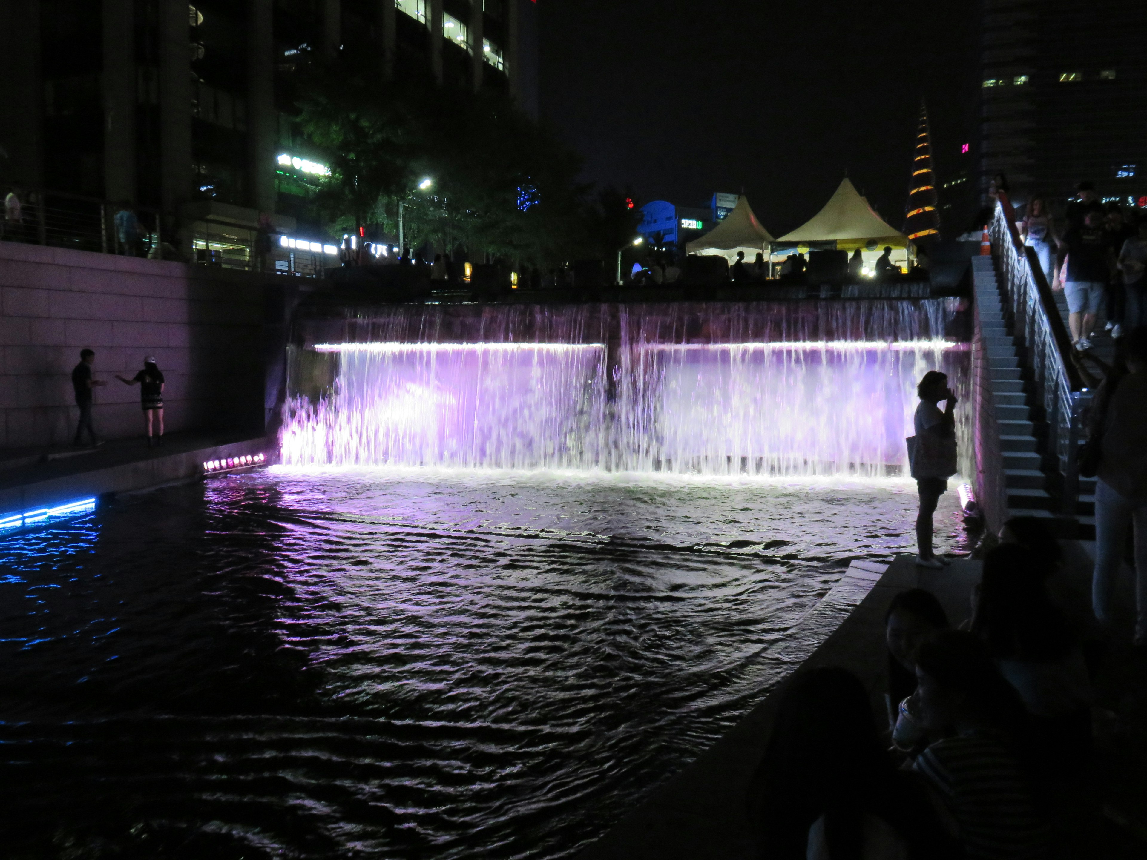 Künstlicher Wasserfall bei Nacht mit buntem Licht und ruhiger Wasseroberfläche