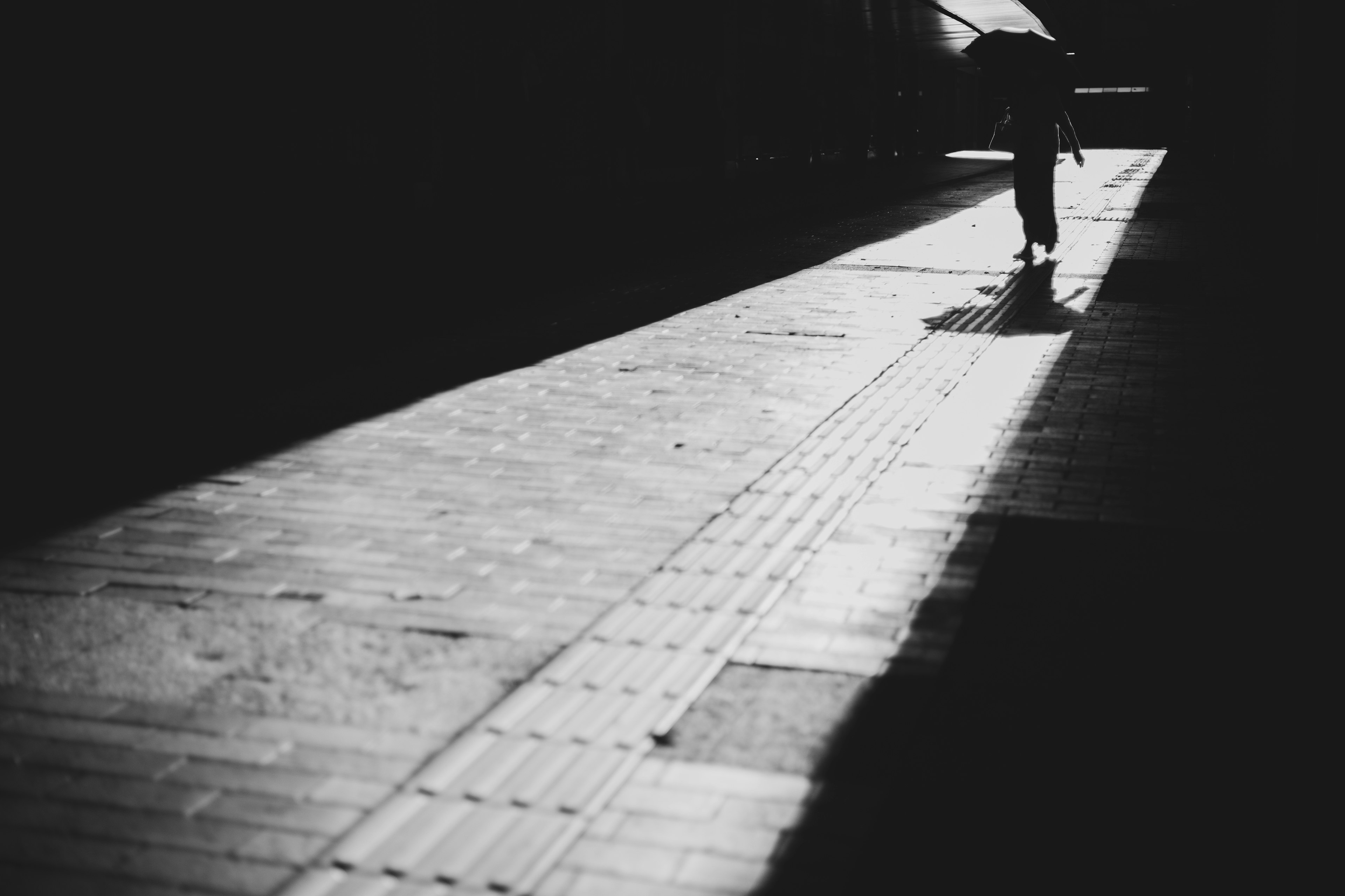 A shadow of a person walking with an umbrella in a dark corridor