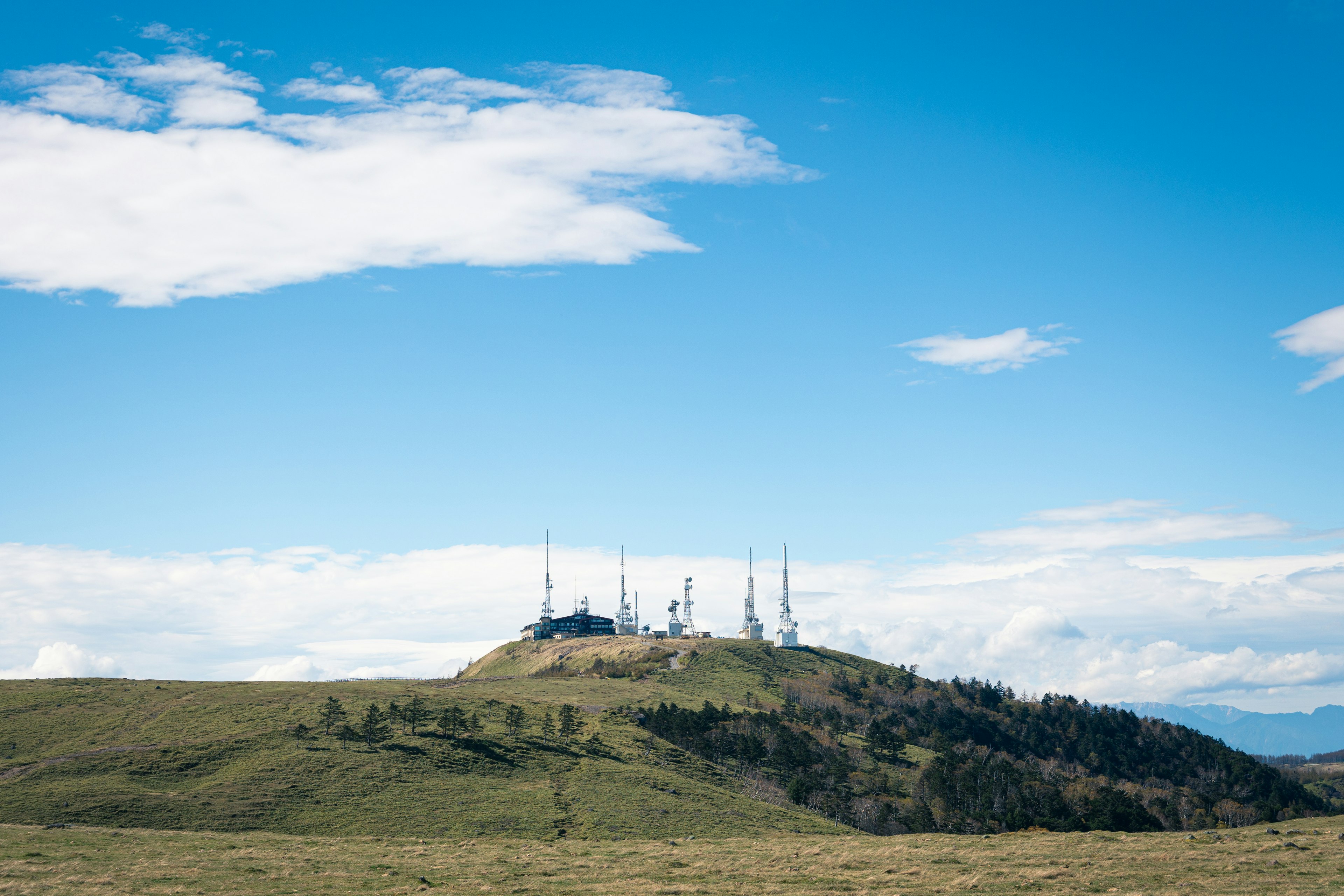 Numerous communication towers atop a high hill under a blue sky