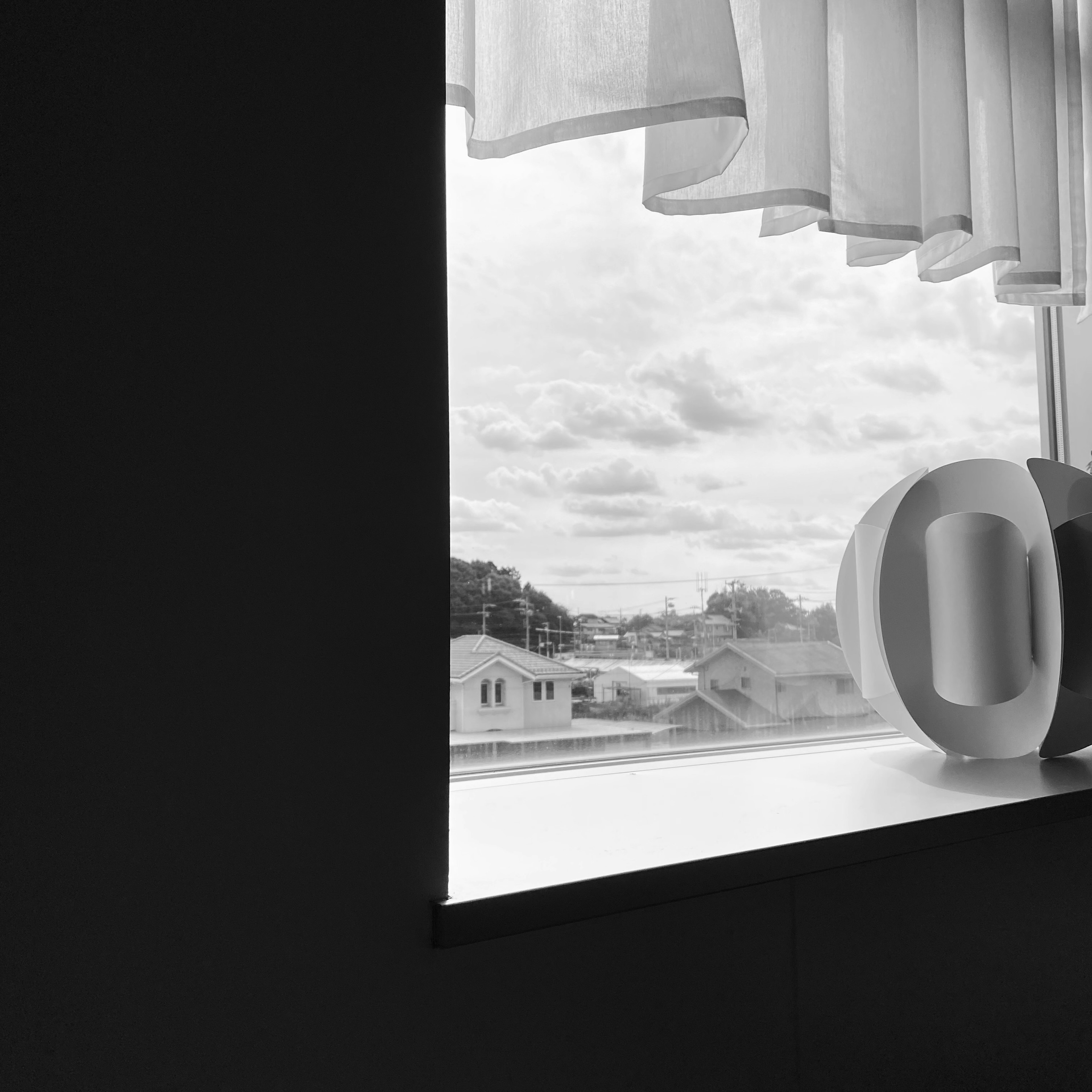 Black and white view of a window with sheer curtains and decorative objects on the sill