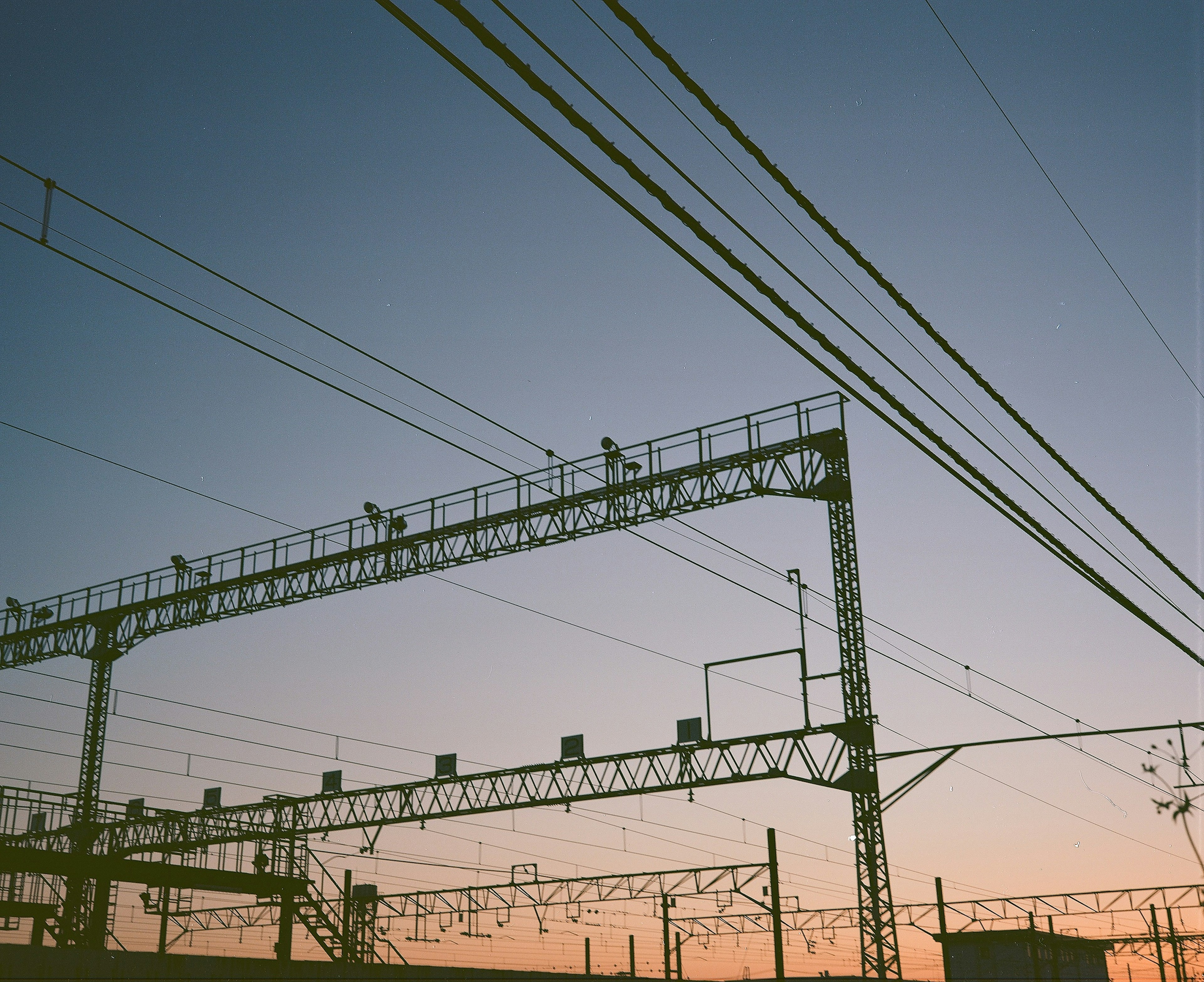 Silhouette von Eisenbahnstromleitungen und Masten vor einem Sonnenuntergangshimmel