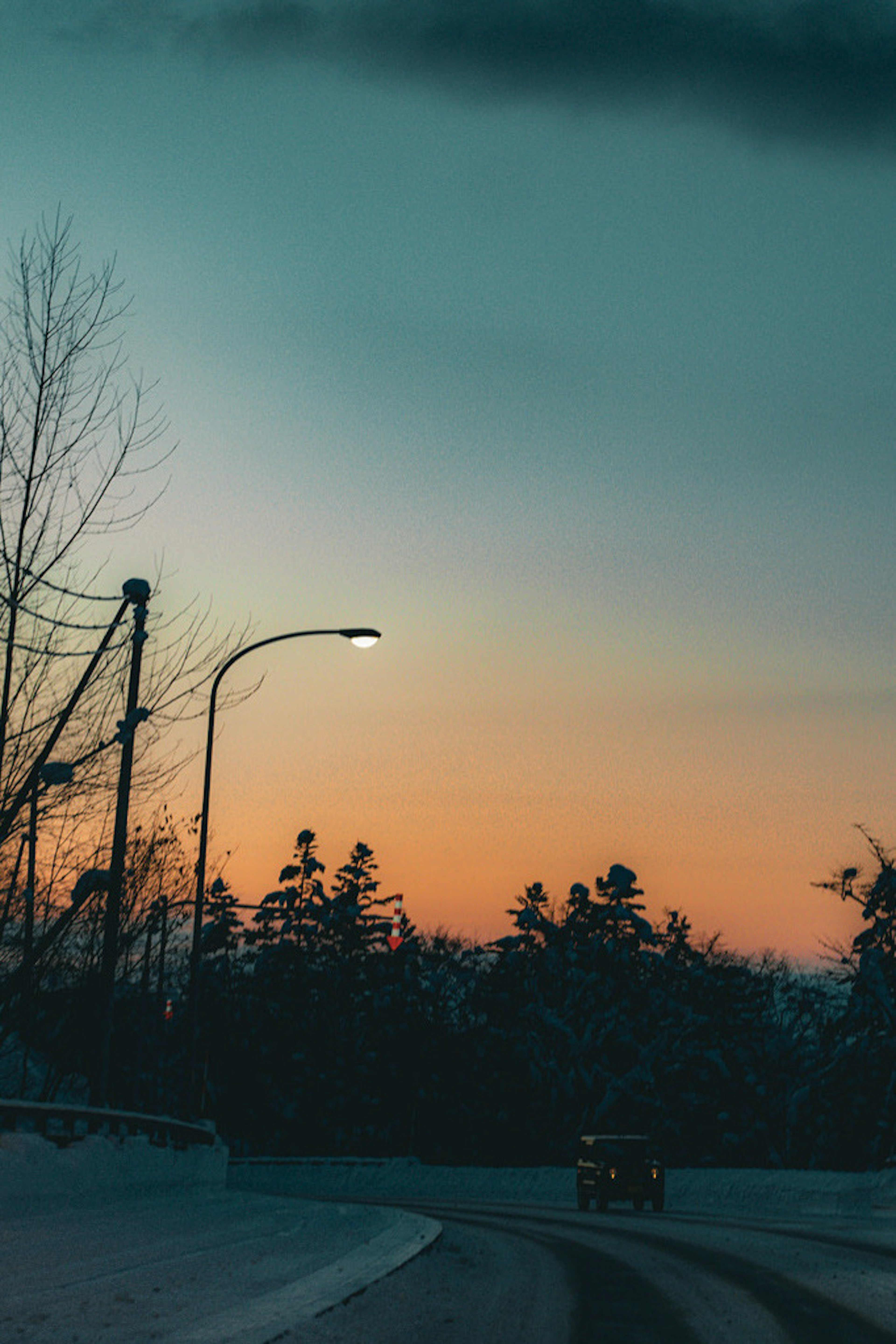 Winterliche Sonnenuntergangsansicht entlang einer Straße mit schneebedeckten Bäumen und orangefarbenem Himmel