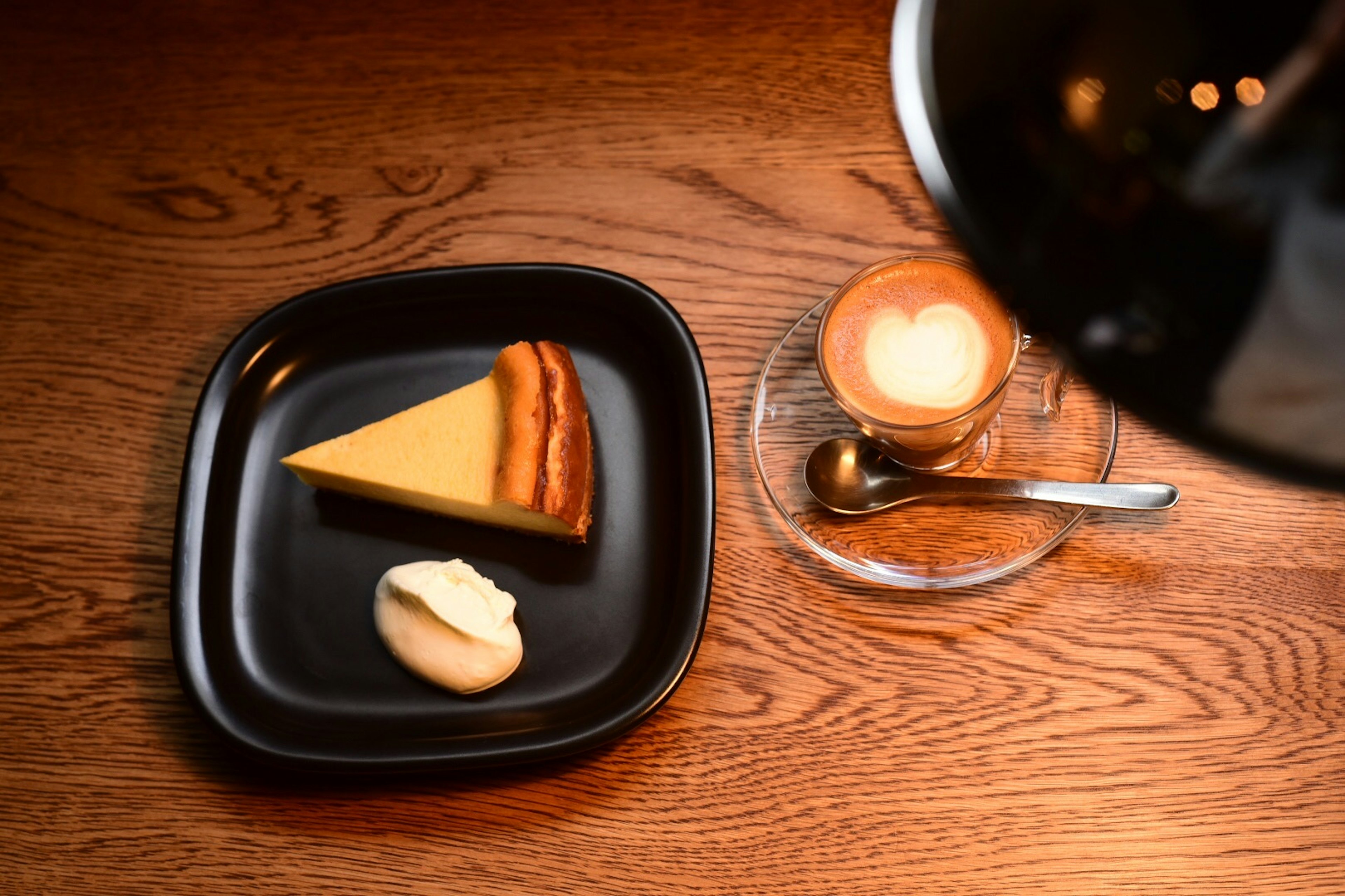 Käsekuchen auf einem schwarzen Teller mit Schlagsahne und einer Kaffeetasse