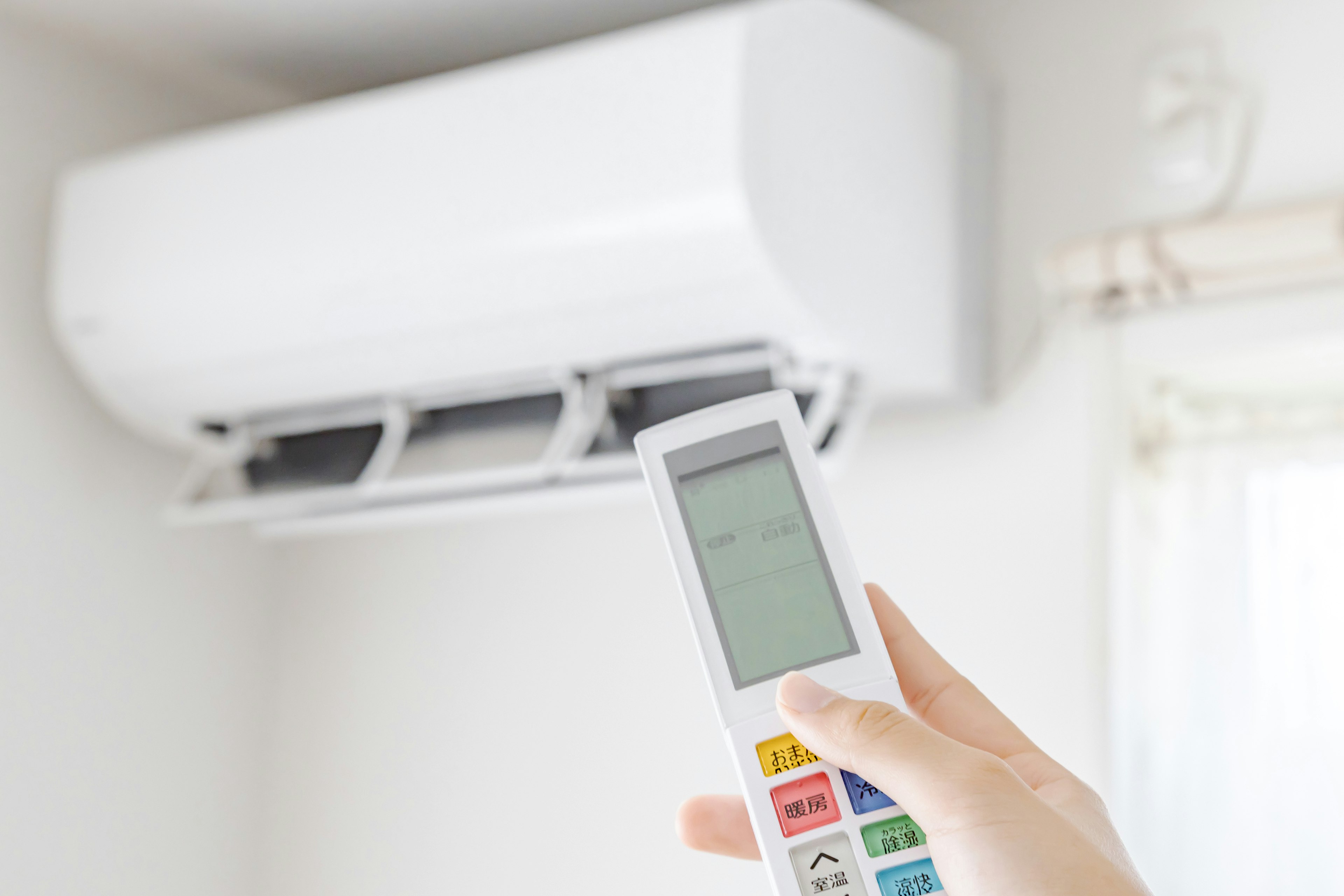 Hand holding air conditioner remote in front of a white air conditioning unit