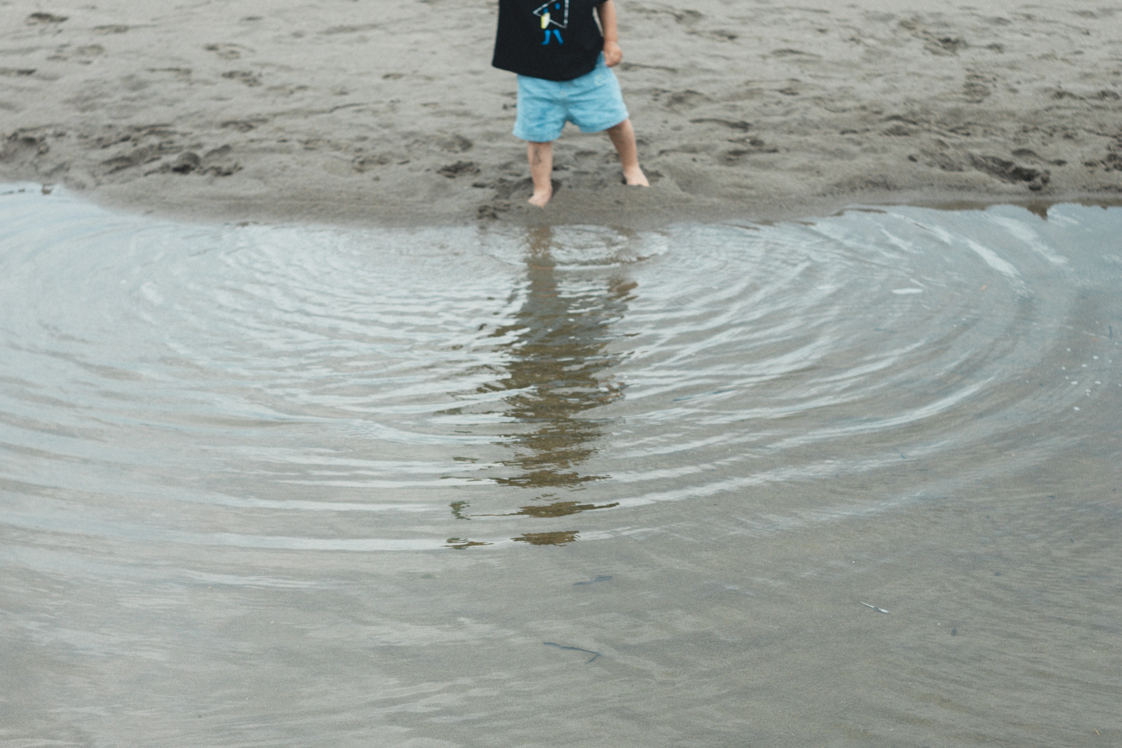 Anak berdiri di air dangkal di pantai