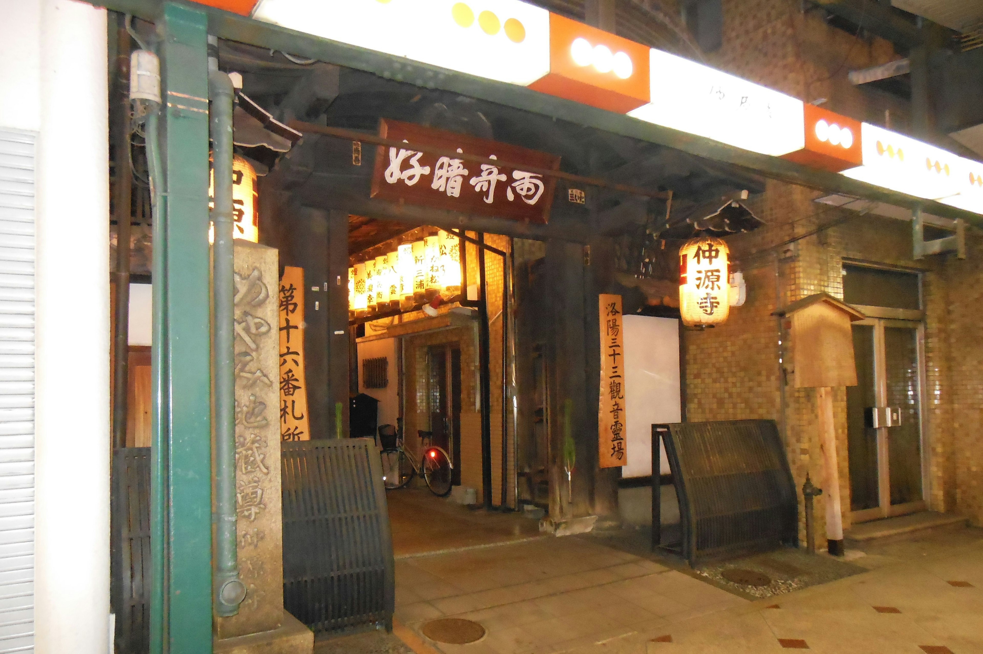 Entrada de un izakaya japonés retro con cartel de madera y luces de farol cálidas