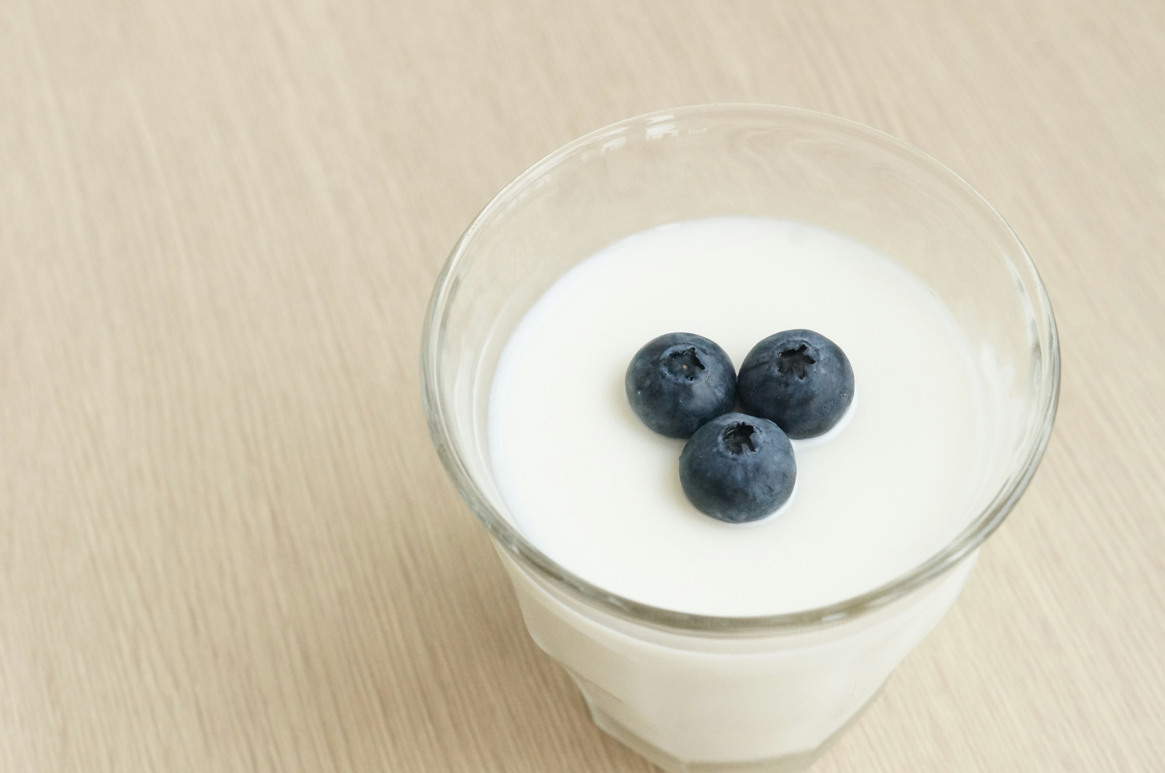 A clear glass containing yogurt topped with three blueberries