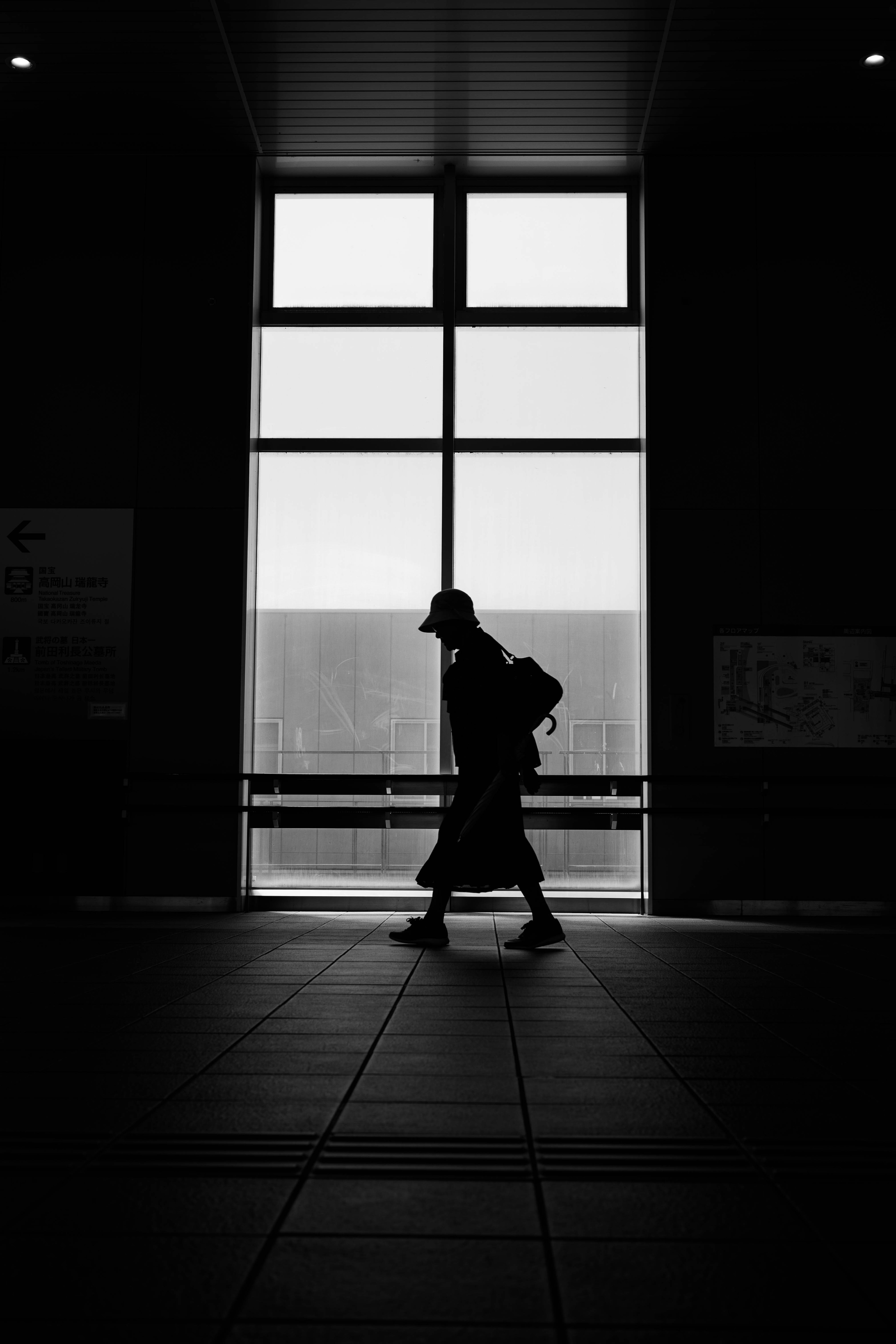 Silhouette d'un homme marchant devant une grande fenêtre en noir et blanc